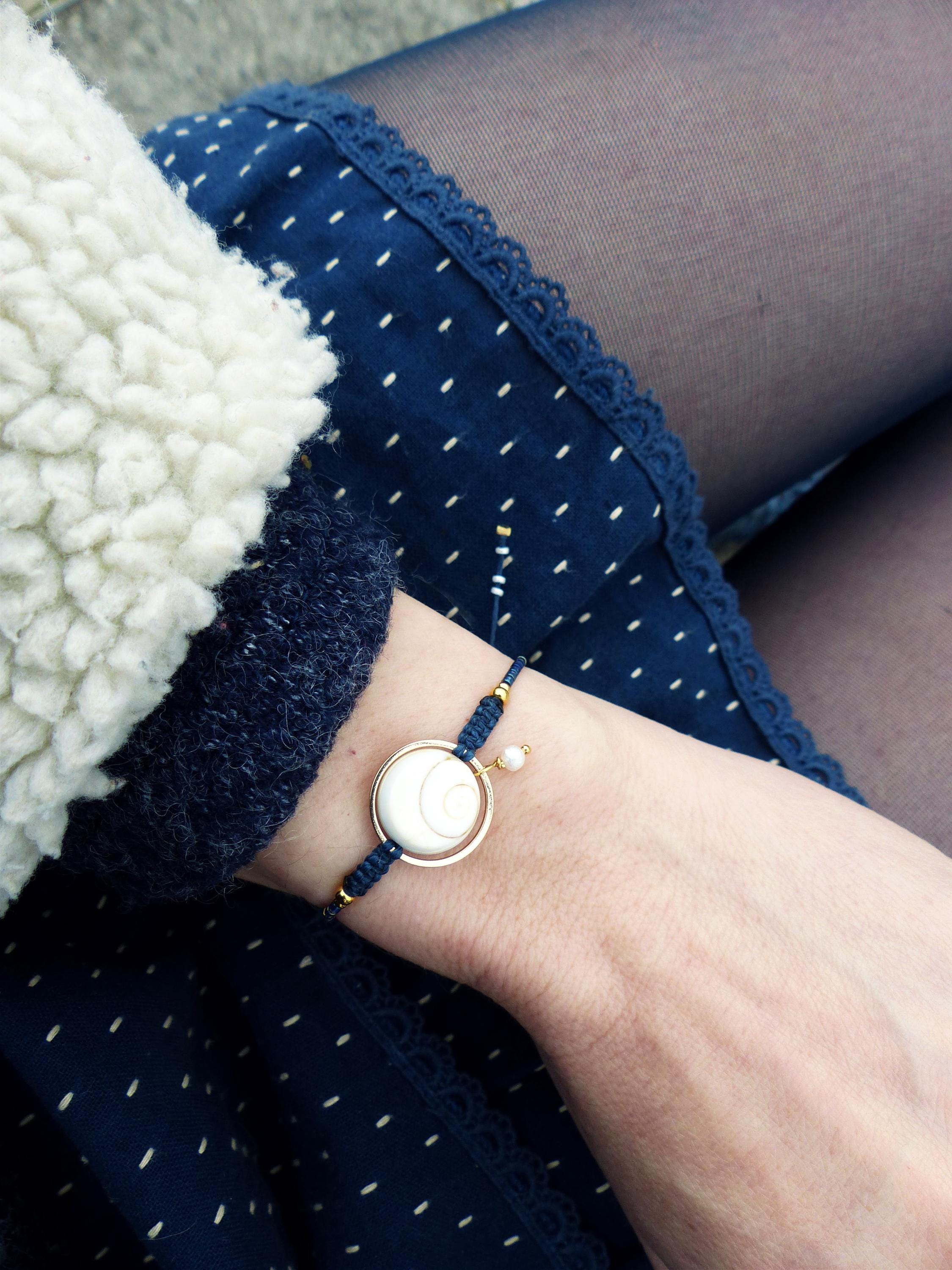 Peut inclure: Un bracelet doré avec un pendentif circulaire blanc orné d'un croissant de lune. Le bracelet est composé d'un cordon bleu marine avec des accents dorés et un petit charme de perle. Le fond comprend une jupe bleu marine à pois blancs.