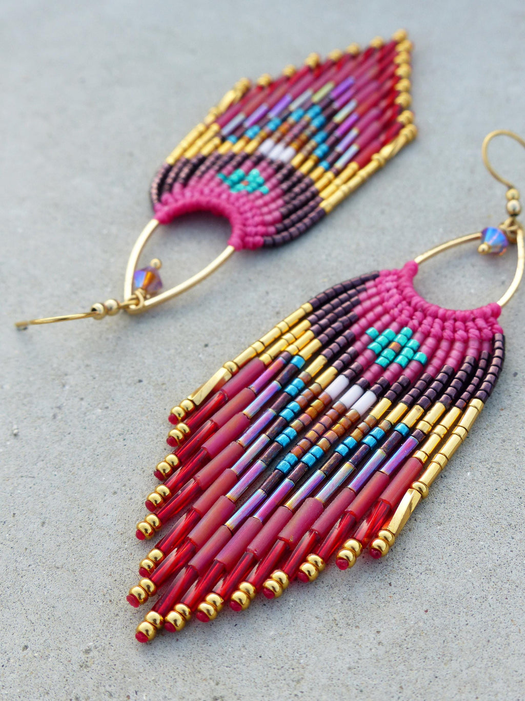 Peut inclure: Boucles d'oreilles faites à la main avec des perles aux couleurs vives. Les boucles d'oreilles présentent une base rose avec des accents dorés et des perles rouges pendantes. Le design incorpore des perles turquoise, violettes et marron.