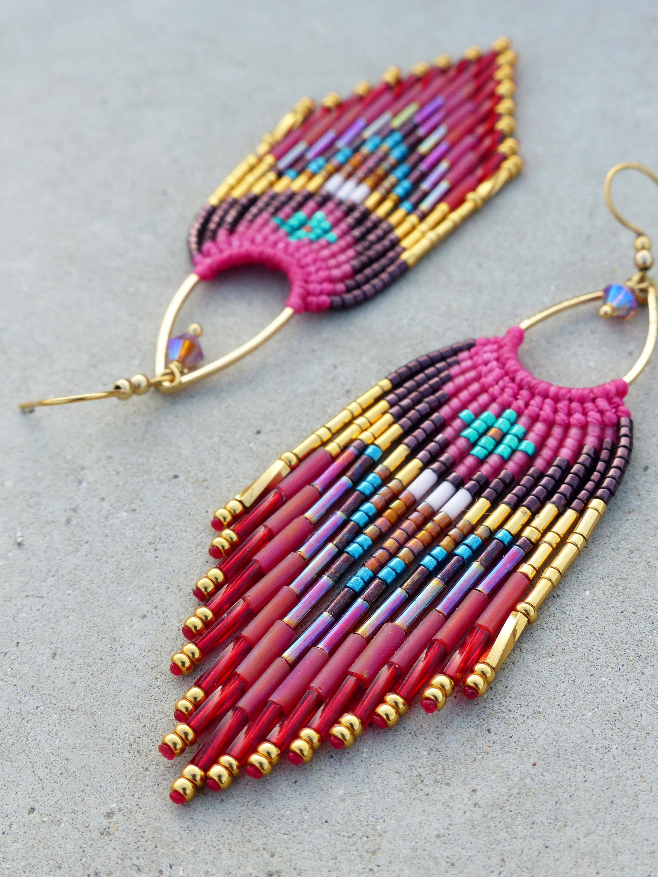 Peut inclure: Boucles d'oreilles faites à la main avec des perles aux couleurs vives. Les boucles d'oreilles présentent une base rose avec des accents dorés et des perles rouges pendantes. Le design incorpore des perles turquoise, violettes et marron.