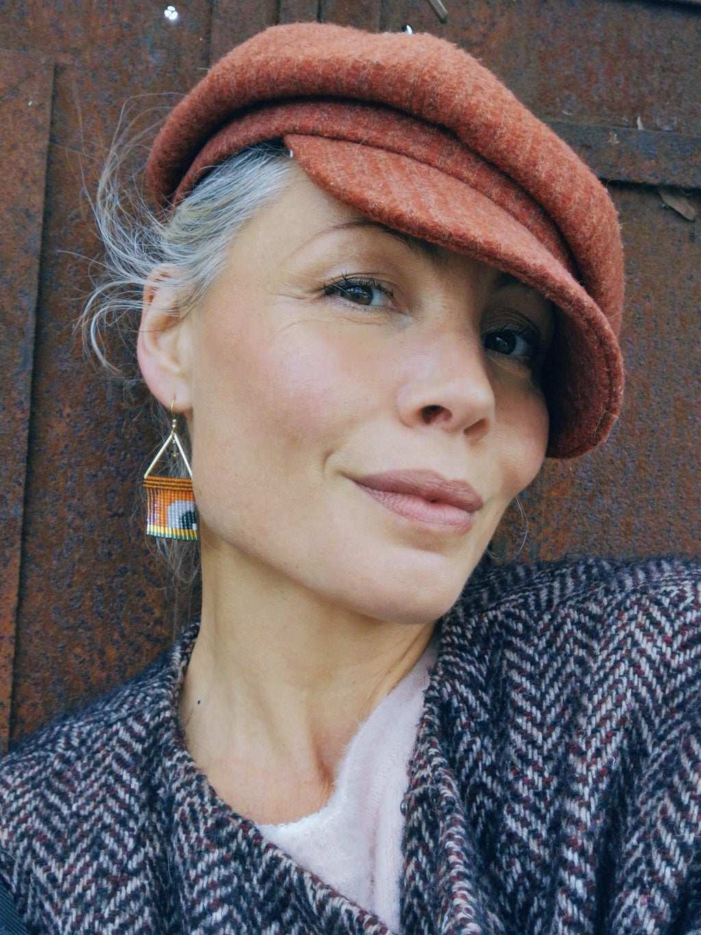 Peut inclure: Une personne portant un béret de couleur rouille et des boucles d'oreilles géométriques. Les boucles d'oreilles ont une forme triangulaire avec des accents orange, jaune et noir. Elle porte également une veste à chevrons.