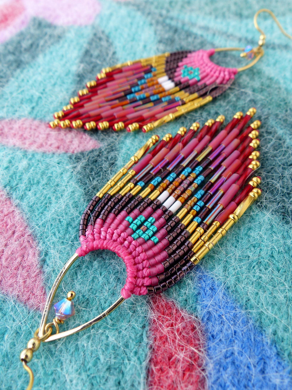 Peut inclure: Gros plan sur deux boucles d'oreilles perlées faites à la main. Les boucles d'oreilles présentent un motif en forme de plume avec des perles roses, rouges, dorées et turquoise. Les boucles d'oreilles sont suspendues à des crochets d'oreilles dorés.