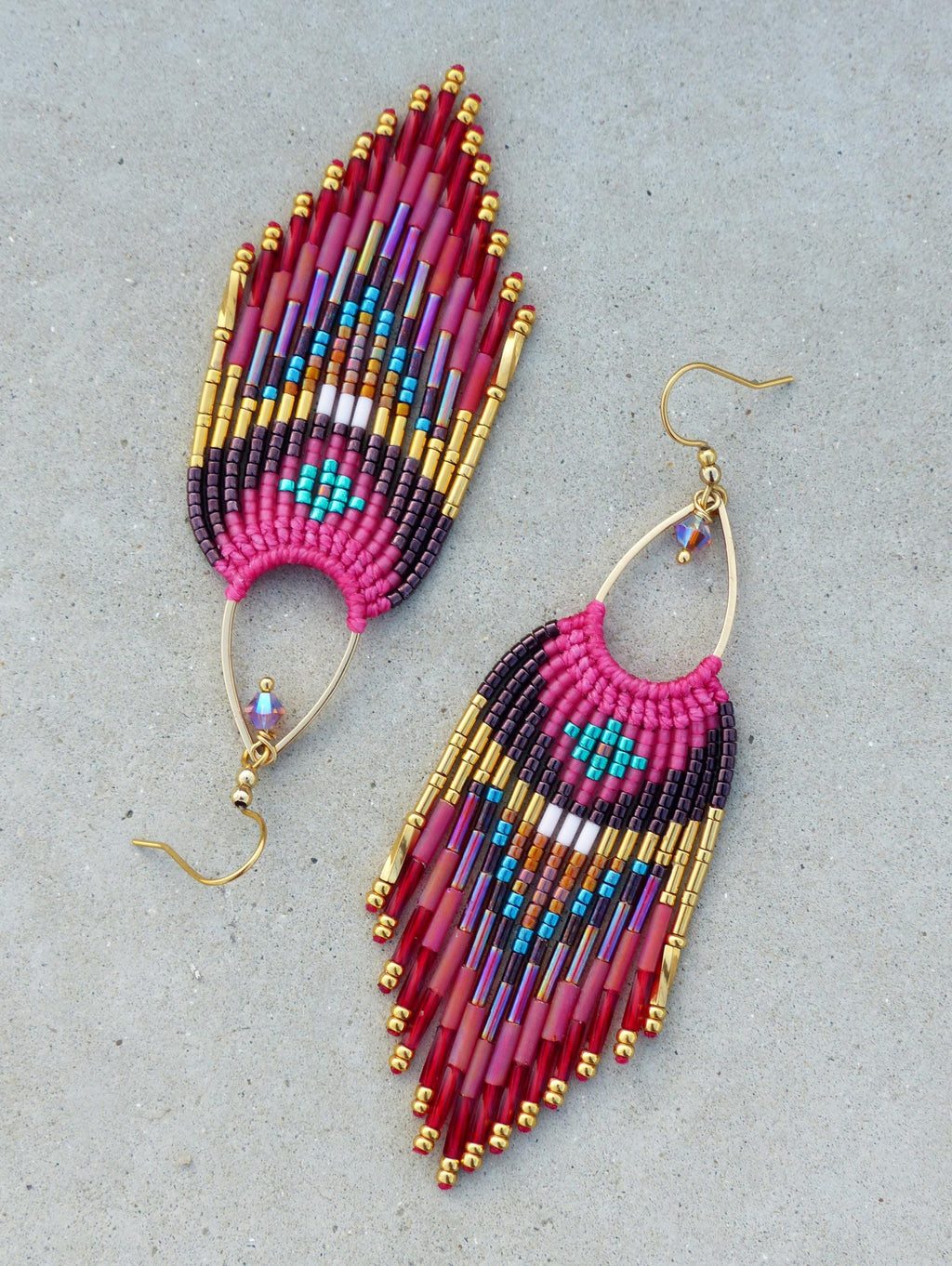 Peut inclure: Paire de boucles d'oreilles faites à la main en forme de plume. Les boucles d'oreilles sont composées de perles rouges, roses, violettes, dorées et turquoise. Elles ont des crochets d'oreilles dorés et un petit cristal.
