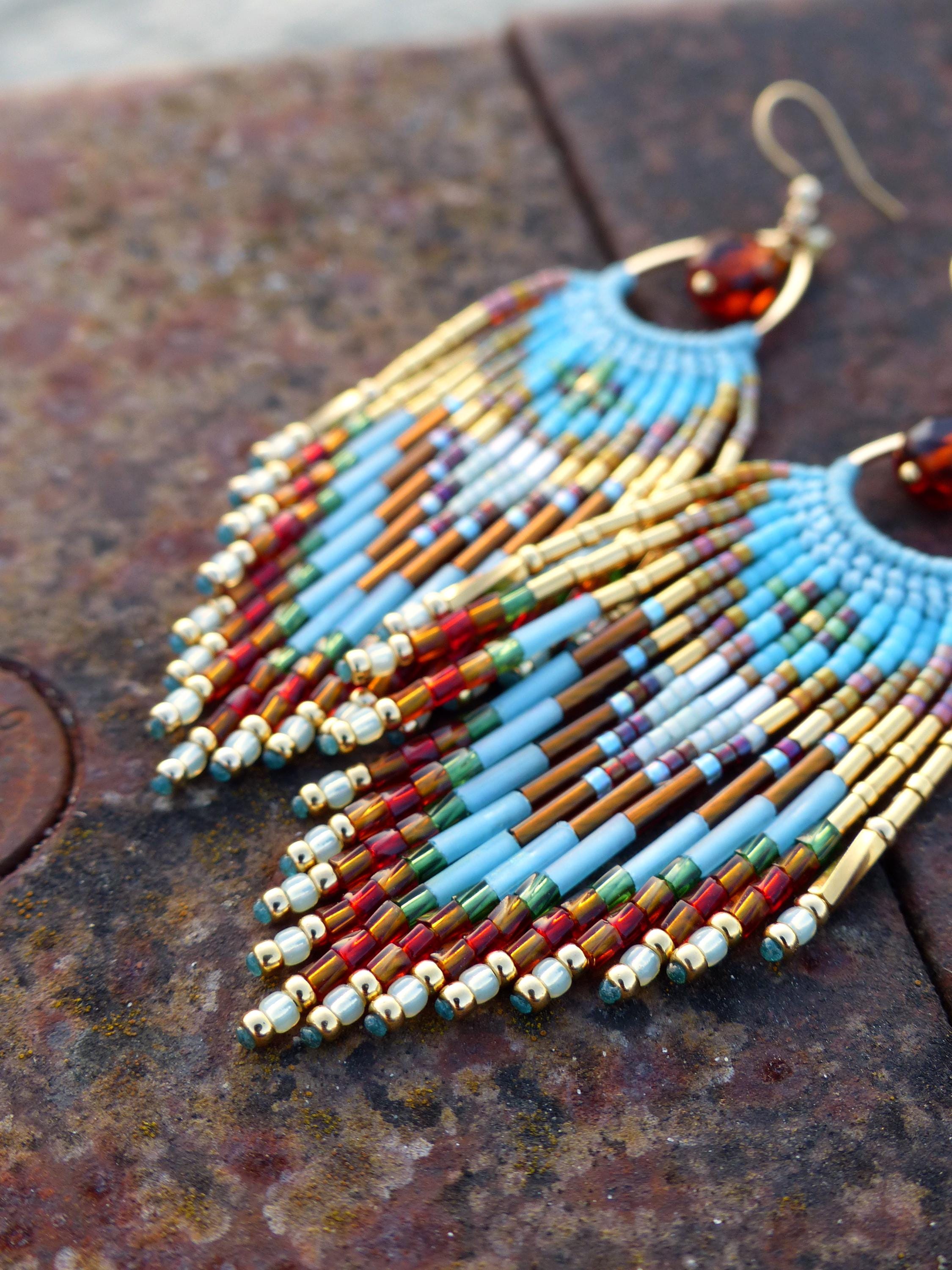Peut inclure: Une paire de boucles d'oreilles perlées faites à la main avec un design à franges. Les boucles d'oreilles présentent une palette de couleurs bleu clair, or, rouge et marron. Les boucles d'oreilles ont un cerceau doré et une petite perle ambrée en haut.