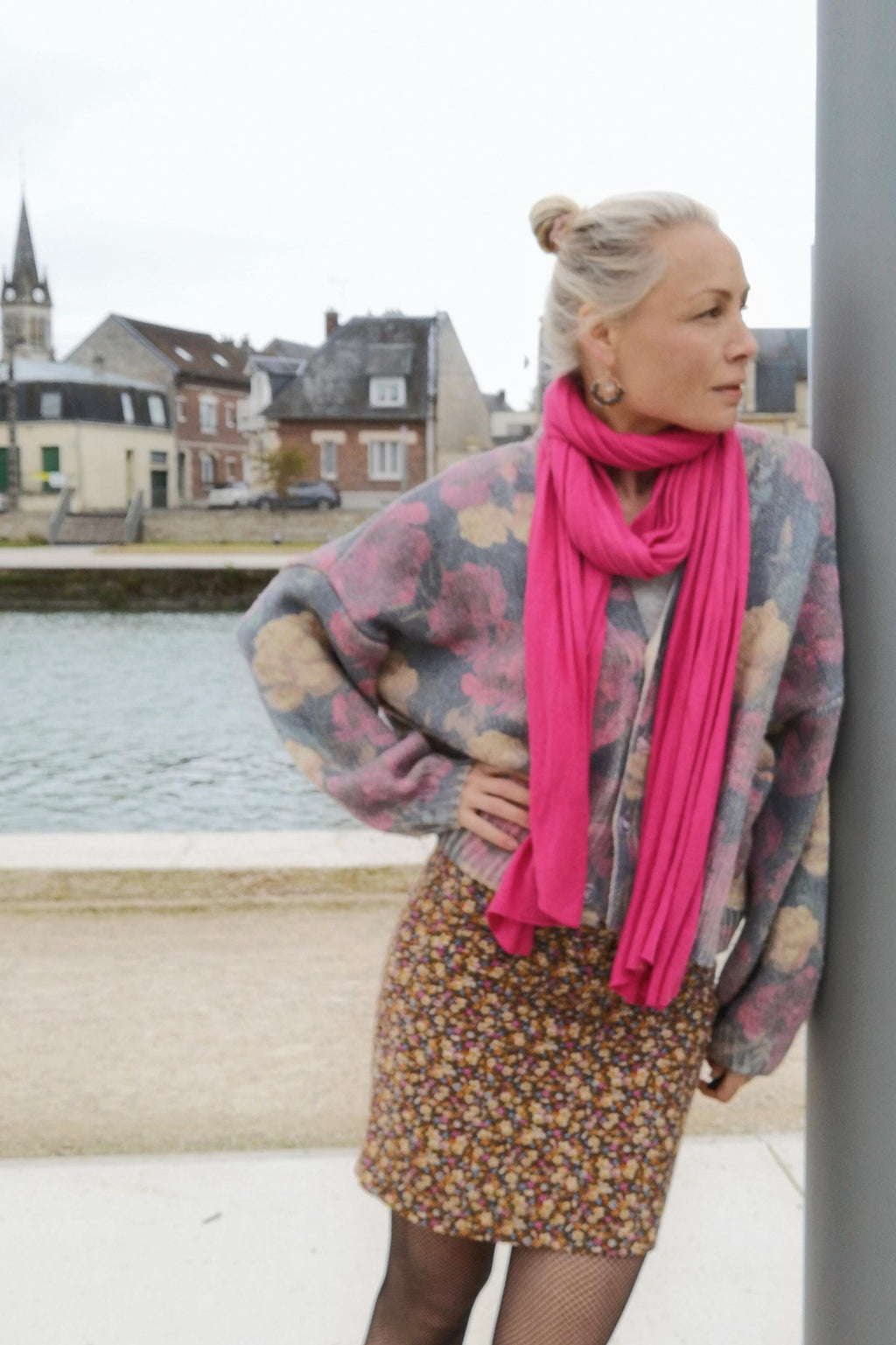 Peut inclure: Une femme porte un cardigan à imprimé floral, une écharpe rose vif et une mini-jupe à imprimé floral. Le cardigan est gris avec des fleurs roses et jaunes. La jupe est marron avec de petites fleurs jaunes et roses. L'écharpe est rose vif.