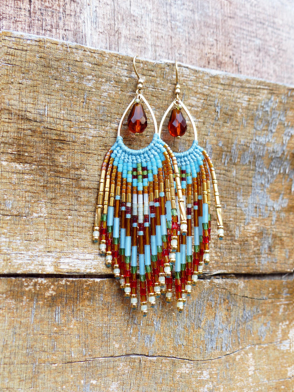 Peut inclure: Boucles d'oreilles faites à la main avec des perles en forme de goutte d'eau. Les boucles d'oreilles présentent une monture en fil doré avec une perle en forme de goutte marron. La frange perlée comprend des perles turquoise, marron, rouges et dorées.