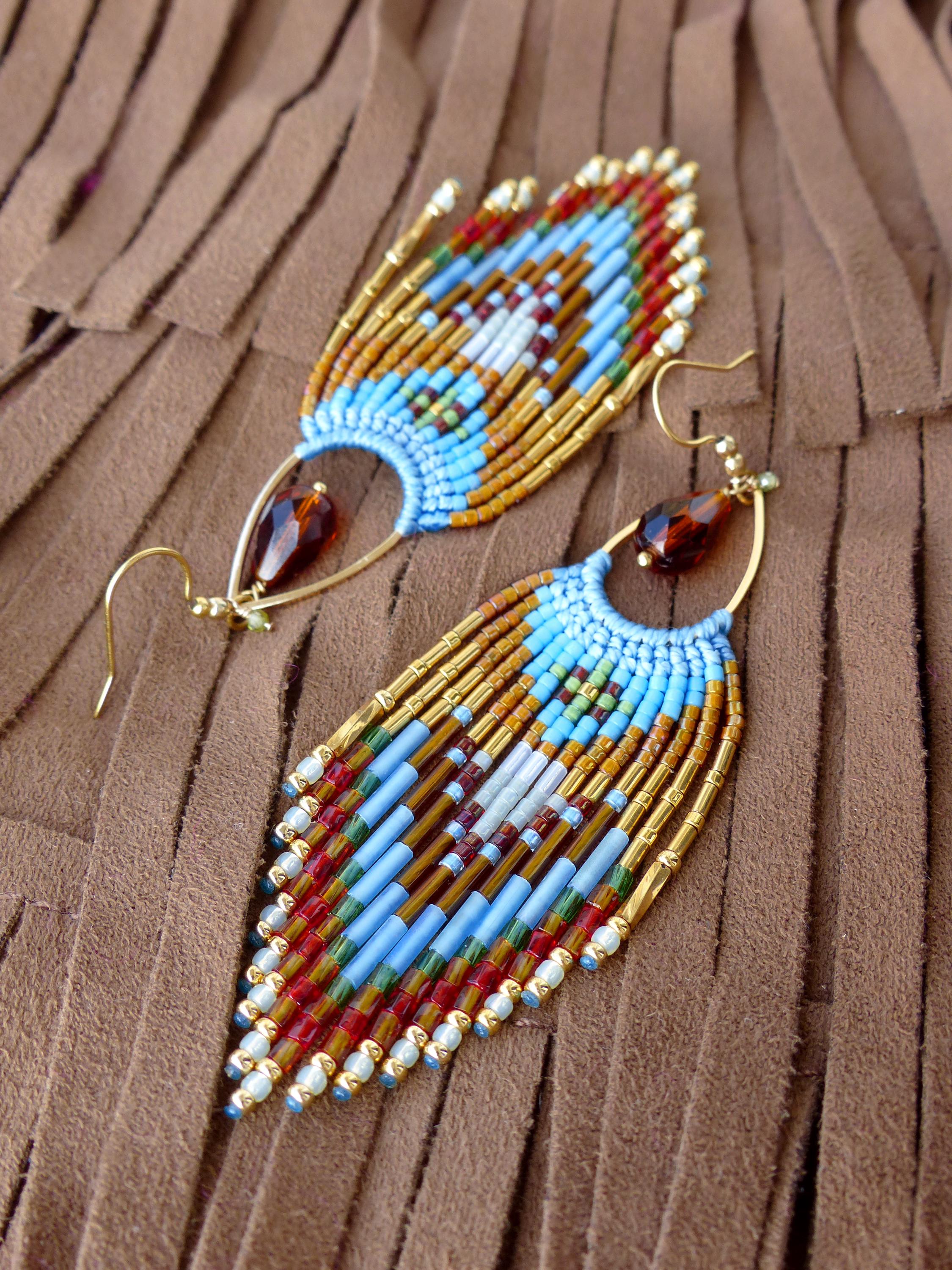 Peut inclure: Paire de boucles d'oreilles faites à la main avec un motif de plumes. Les boucles d'oreilles sont composées de perles bleues, rouges, blanches et dorées. Chaque boucle d'oreille a une perle ambrée en forme de goutte et des crochets d'oreilles dorés.