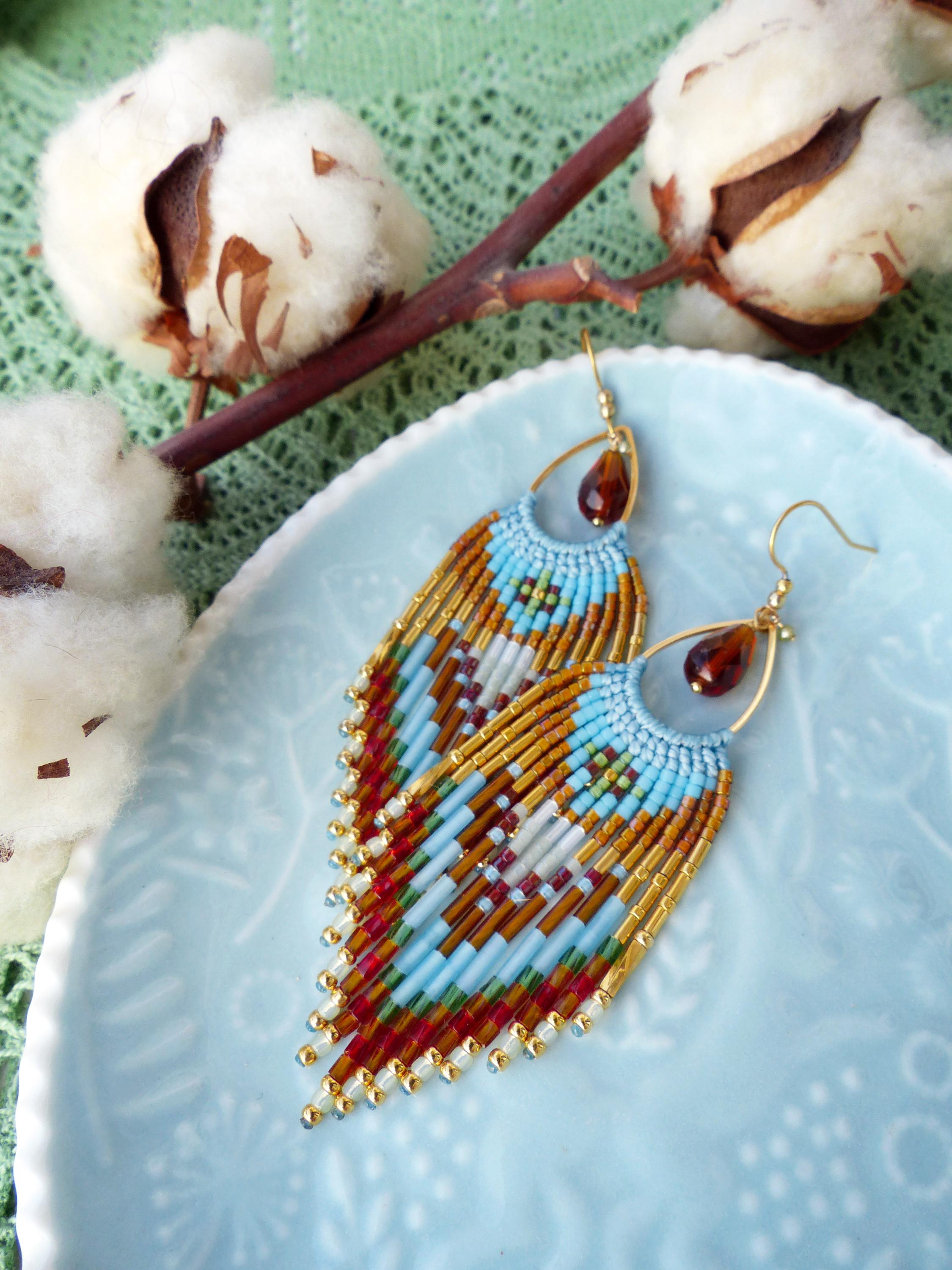 Peut inclure: Paire de boucles d'oreilles faites à la main avec des crochets dorés et des perles en forme de goutte ambrée. Les boucles d'oreilles présentent un motif géométrique dans les tons de bleu, rouge, marron et or, avec un design à franges.