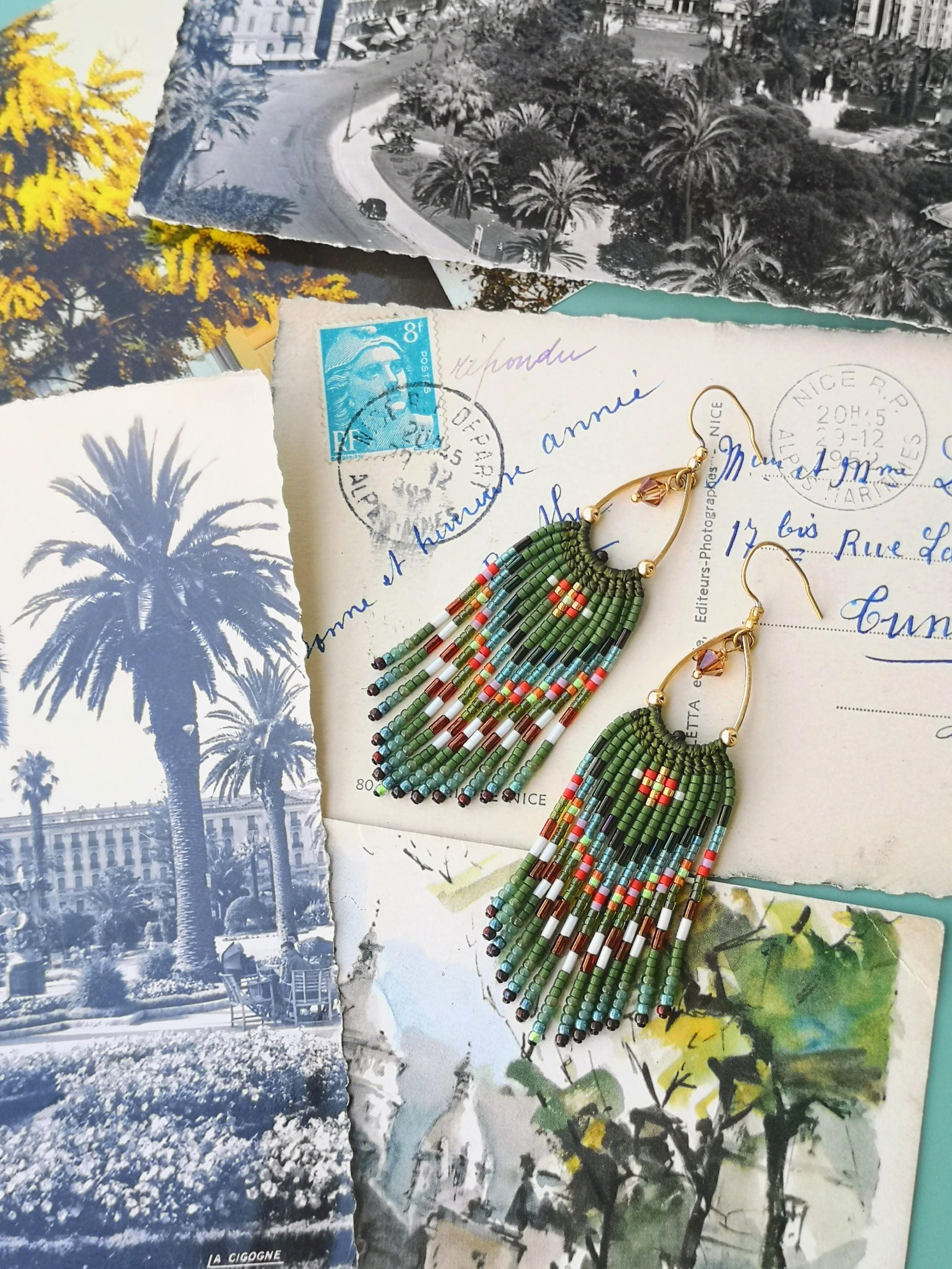 Peut inclure: Boucles d'oreilles faites à la main avec un design à franges. Les boucles d'oreilles ont une base verte avec des accents rouges, blancs et bleus. Elles sont présentées sur des cartes postales vintage.