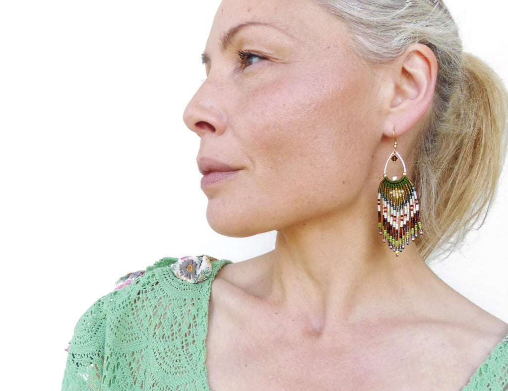 Peut inclure: Boucles d'oreilles pendantes dorées avec un motif de franges perlées. Les boucles d'oreilles présentent un mélange de perles vertes, marron, blanches et rouges, créant un motif géométrique texturé. Un bijou audacieux pour ajouter de la couleur et de la texture.