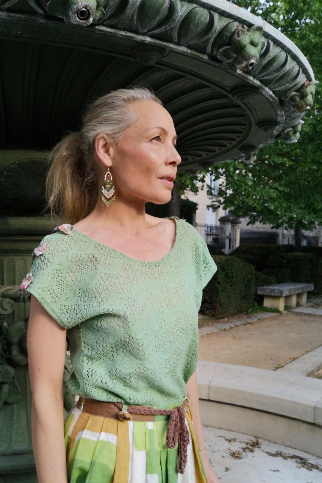 Peut inclure: Un haut vert clair à manches courtes avec un motif de dentelle délicat. La tenue comprend une jupe à rayures et carreaux jaunes, blancs et verts. Une ceinture marron souligne la taille. Des boucles d'oreilles dorées et vertes complètent l'ensemble.