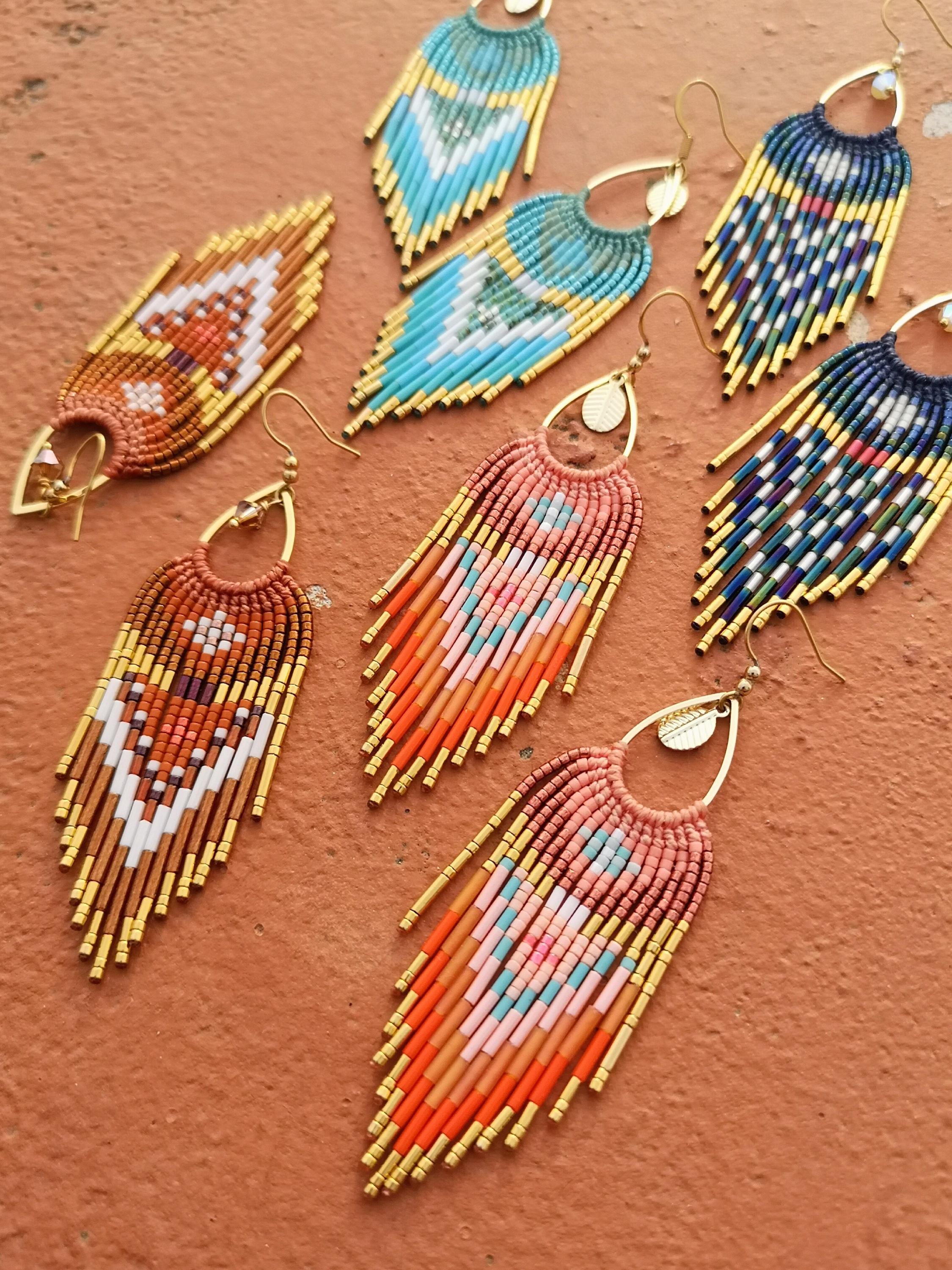 Peut inclure: Une collection de boucles d'oreilles perlées faites à la main de différentes couleurs. Les boucles d'oreilles présentent des motifs complexes et des détails de franges, avec des accents métalliques dorés. Les couleurs incluent le turquoise, l'orange, le rose et le marron.
