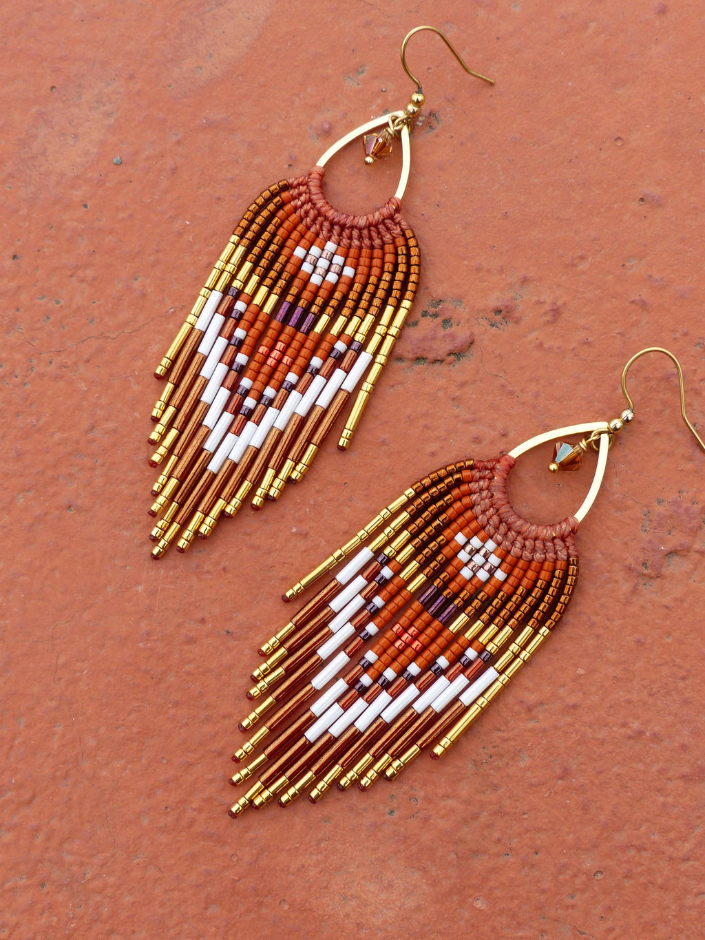 Peut inclure: Boucles d'oreilles faites à la main avec des perles en forme de goutte d'eau. Les boucles d'oreilles présentent un motif de perles blanches, dorées et marron, avec une frange de perles en bas. Les boucles d'oreilles ont des crochets d'oreilles dorés.
