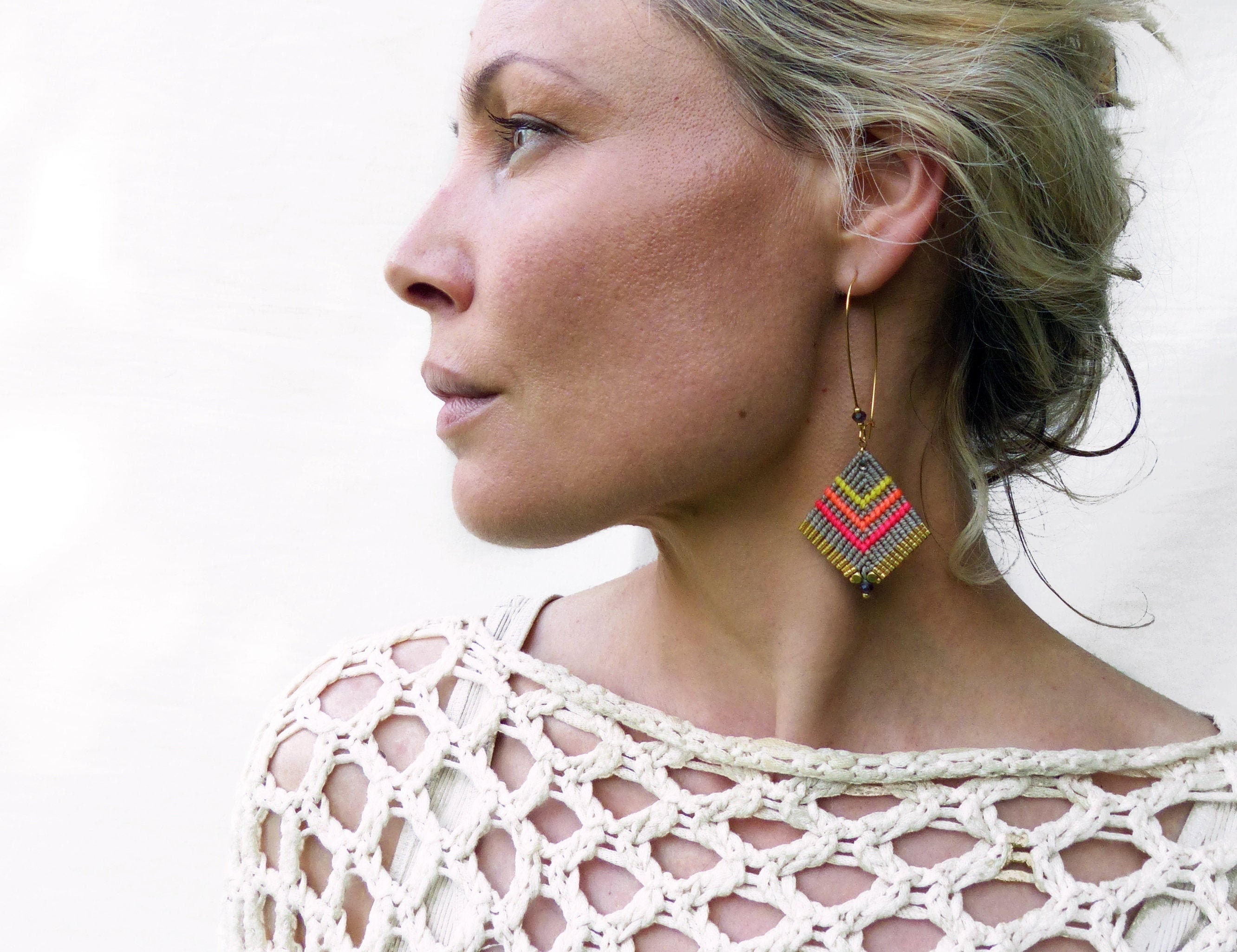 Peut inclure: Une femme portant un haut en crochet blanc avec une paire de longues boucles d'oreilles pendantes. Les boucles d'oreilles sont faites de fil gris, jaune et rose et ont un design géométrique.
