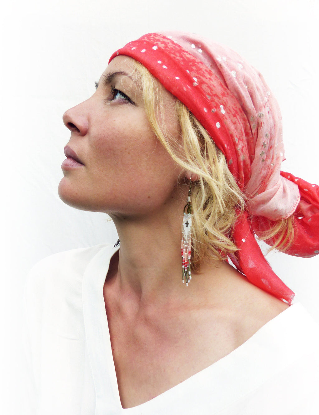 Peut inclure: Une femme porte un foulard rouge et rose à pois blancs et de longues boucles d'oreilles perlées. Les boucles d'oreilles ont un motif de croix et des perles rouges, blanches et argentées. Elle porte un haut blanc.
