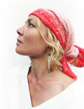 Peut inclure: Une femme porte un foulard rouge et rose à pois blancs et de longues boucles d'oreilles perlées. Les boucles d'oreilles ont un motif de croix et des perles rouges, blanches et argentées. Elle porte un haut blanc.