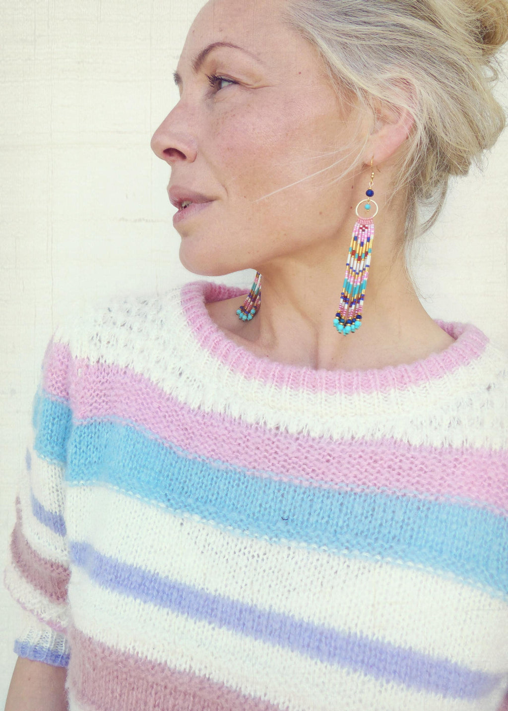 Peut inclure: Un pull à rayures pastel blanc, rose, bleu et lavande est porté avec de longues boucles d'oreilles perlées. Les boucles d'oreilles ont un cercle doré et une longue frange de perles colorées dans les tons de rose, bleu, jaune et turquoise.