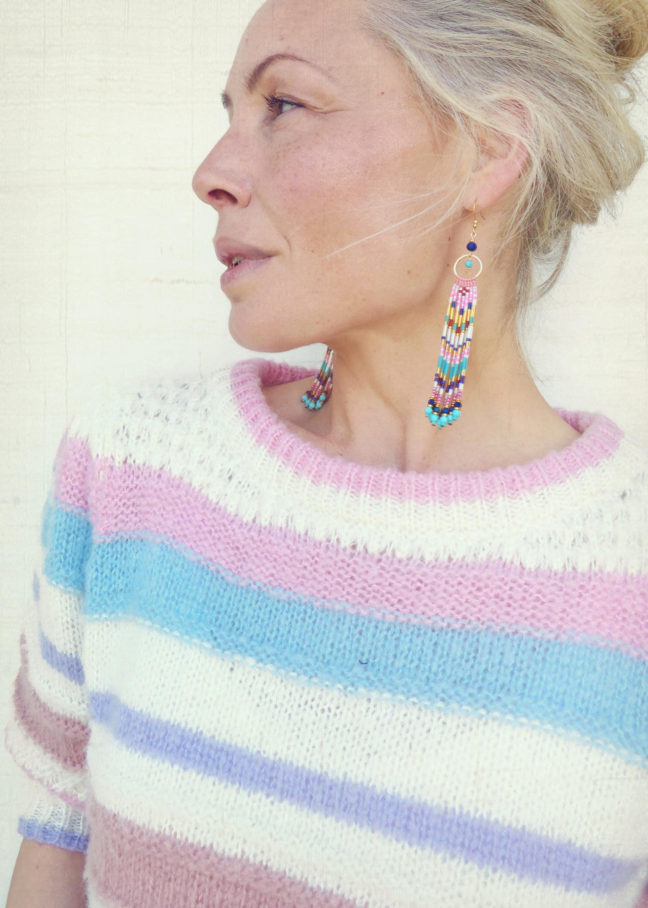 Peut inclure: Un pull à rayures pastel blanc, rose, bleu et lavande est porté avec de longues boucles d'oreilles perlées. Les boucles d'oreilles ont un cercle doré et une longue frange de perles colorées dans les tons de rose, bleu, jaune et turquoise.
