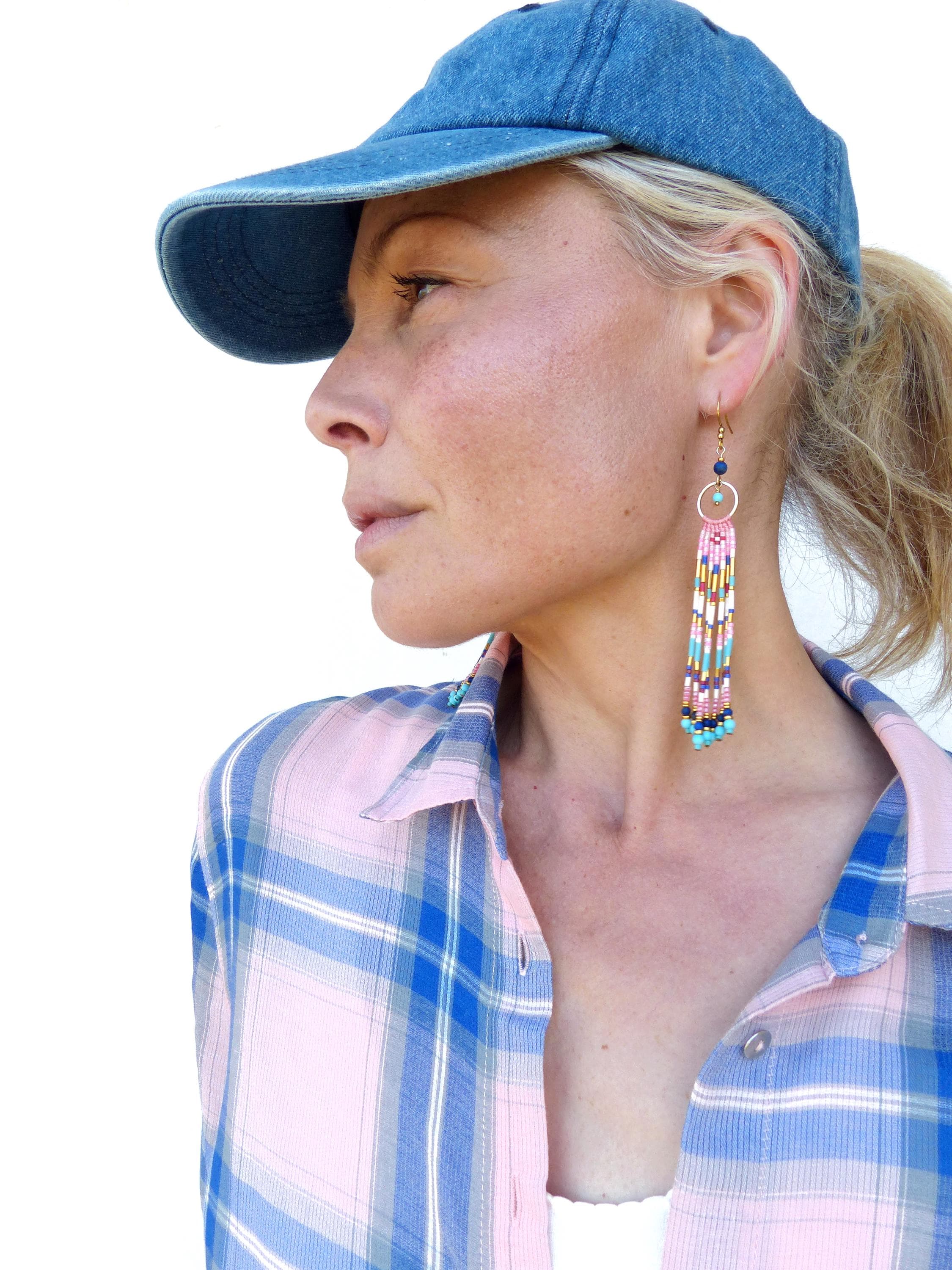 Peut inclure: Casquette de baseball en jean et chemise à carreaux rose et bleu. L'image présente une paire de longues boucles d'oreilles en perles avec un anneau doré et des franges colorées dans les tons rose, bleu et jaune. Les boucles d'oreilles sont un accessoire saisissant.