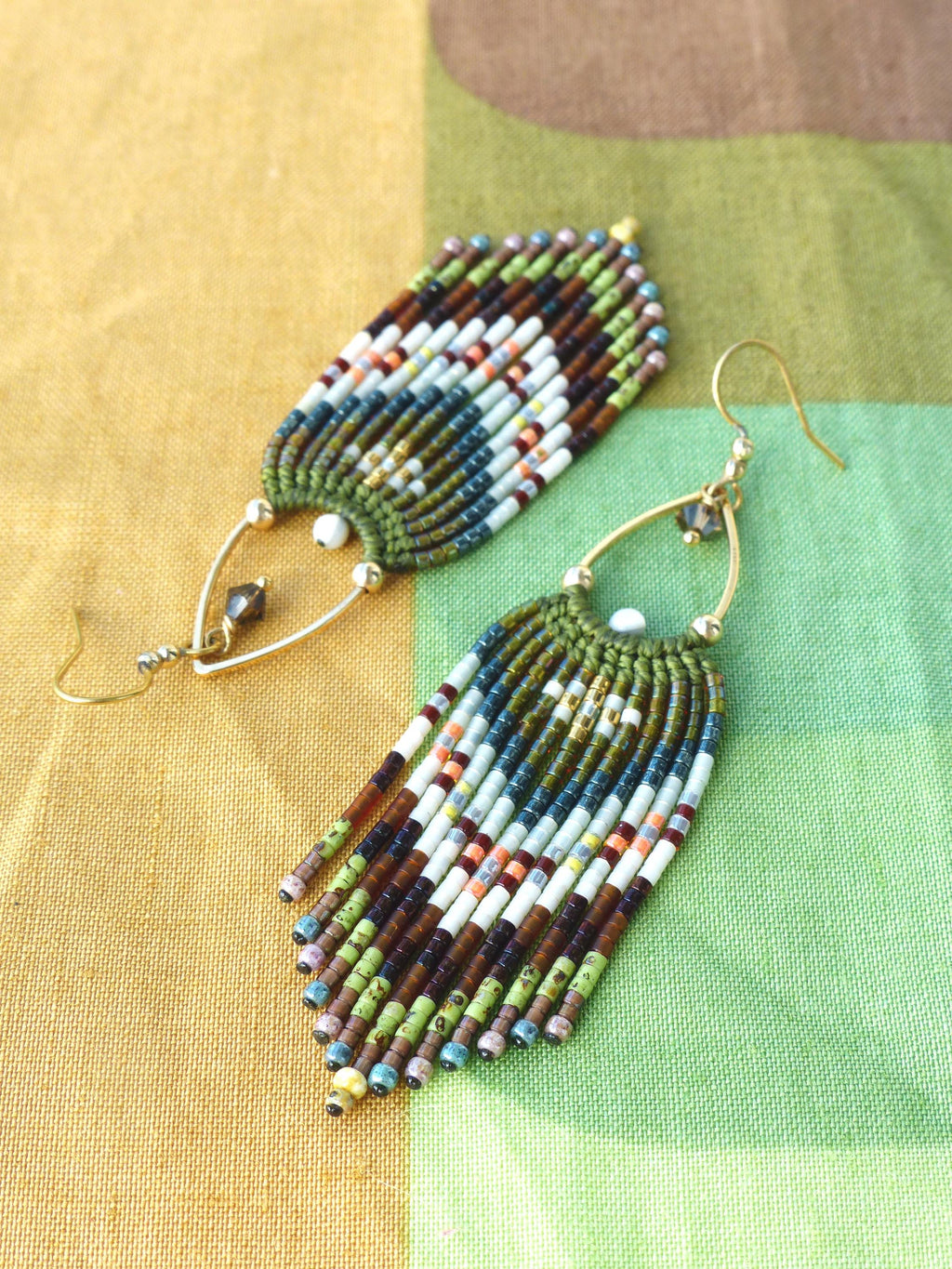 Peut inclure: Une paire de boucles d'oreilles faites à la main avec un design à franges. Les boucles d'oreilles présentent un mélange de couleurs, notamment des perles vertes, marron, blanches, bleues et orange. Les boucles d'oreilles ont des crochets d'oreilles dorés.