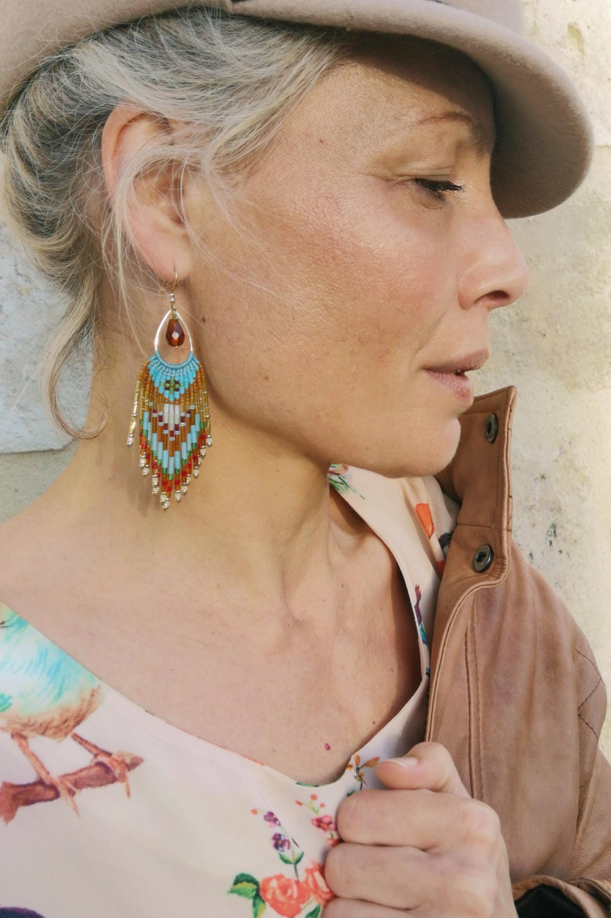 Peut inclure: Boucles d'oreilles pendantes en perles avec une partie supérieure en forme de goutte d'eau et un design à longues franges. Les boucles d'oreilles présentent une palette de couleurs turquoise, orange, blanc et or, créant un accessoire vibrant. 