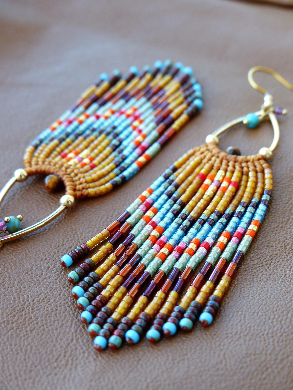 Peut inclure: Gros plan sur deux boucles d'oreilles faites à la main. Les boucles d'oreilles ont des crochets en métal doré et des bases tissées. La frange de perles est un mélange de couleurs, dont le bleu, l'orange, le jaune et le marron. Les boucles d'oreilles sont sur une surface marron.