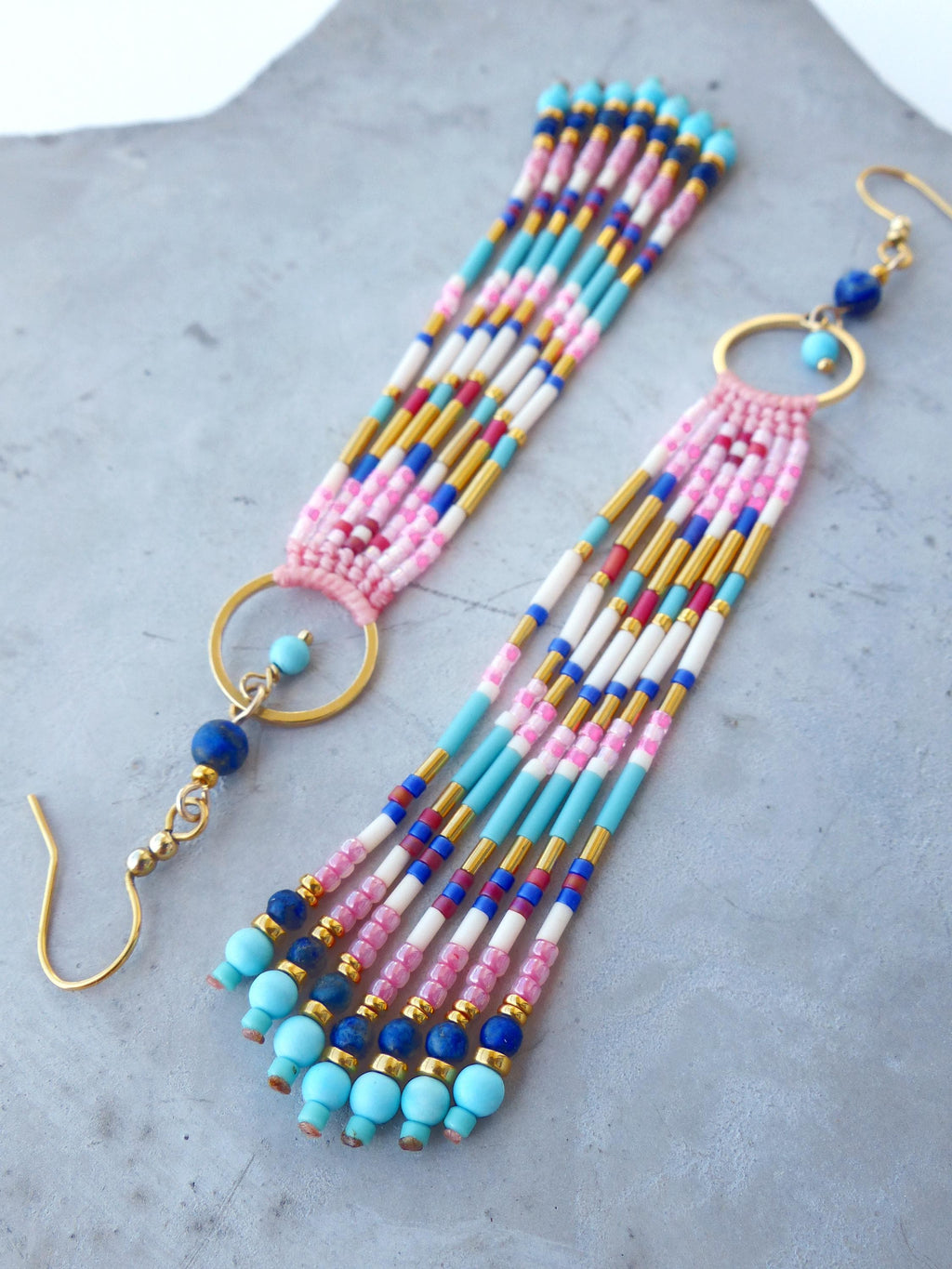 Peut inclure: Boucles d'oreilles faites à la main avec un design coloré. Elles présentent des perles roses, bleues, blanches et dorées, disposées en franges. Les boucles d'oreilles ont des anneaux et des crochets d'oreilles dorés. Le design est complexe et attrayant.