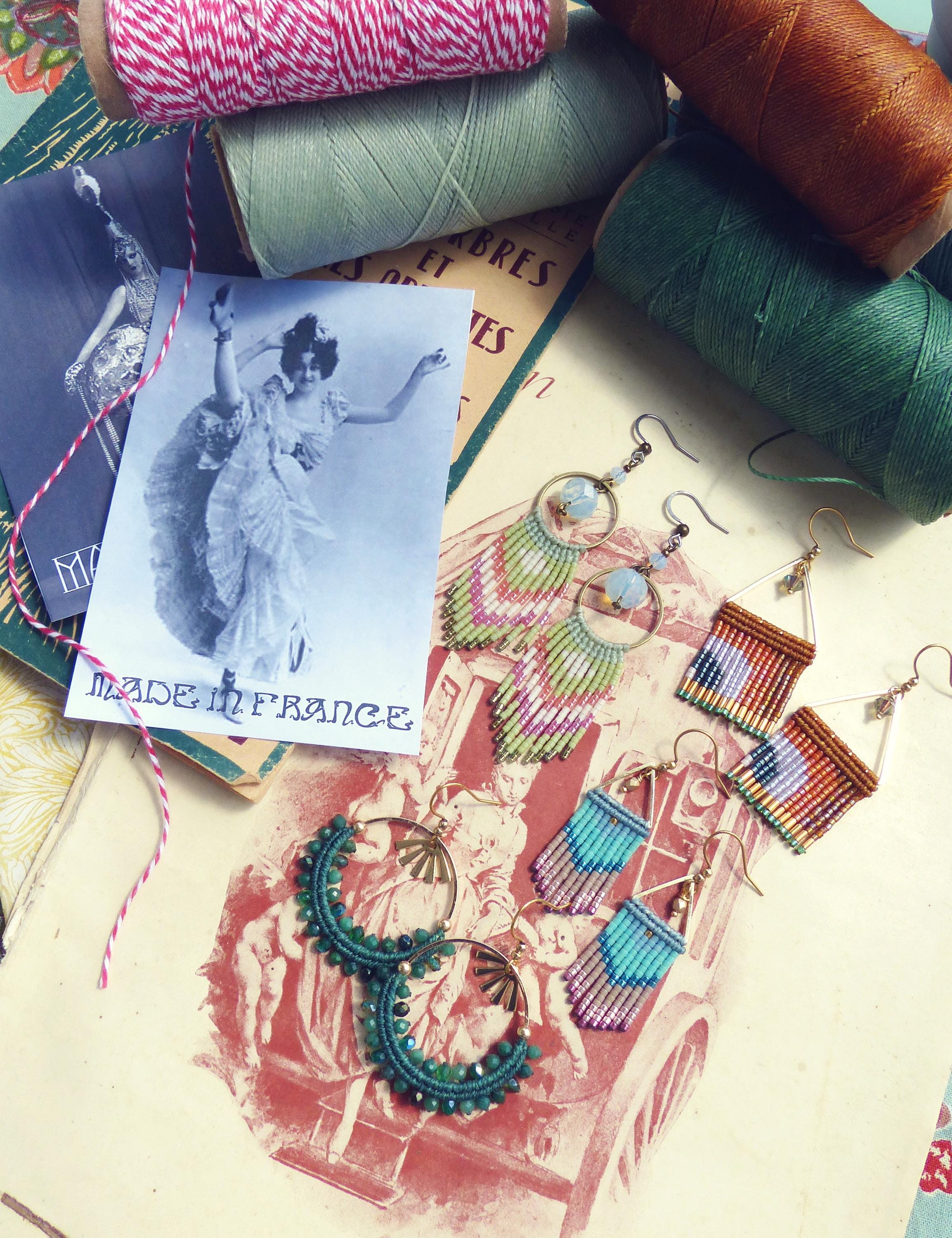 Peut inclure: Diverses boucles d'oreilles faites à la main, aux styles et couleurs variés, dont des créations en macramé et perlées. L'image présente également des bobines de fil, des objets éphémères vintage et une étiquette « MADE IN FRANCE ».