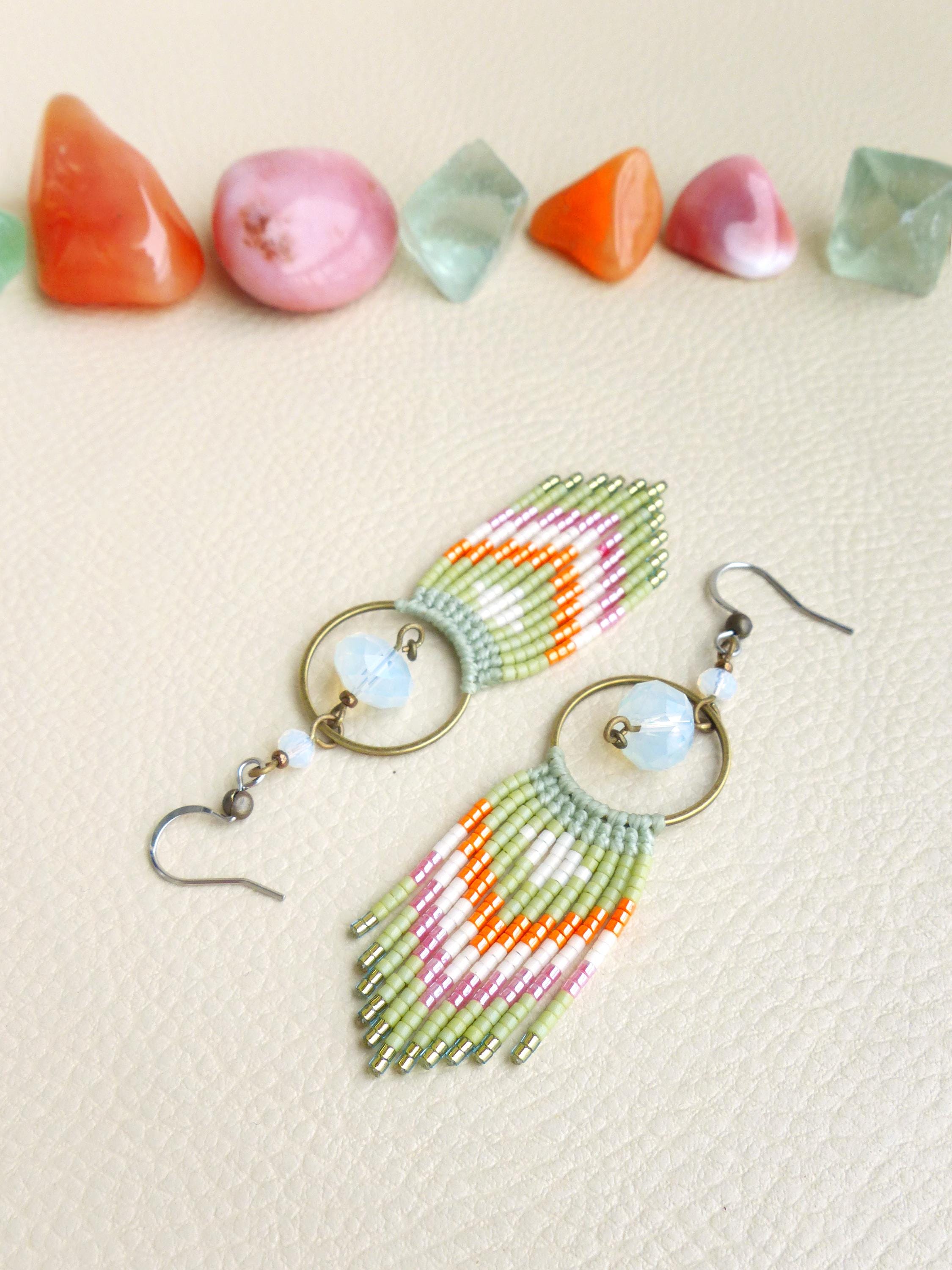 Peut inclure: Boucles d'oreilles macramé faites à la main avec un motif vert, blanc, orange et rose. Les boucles d'oreilles ont un anneau circulaire en laiton et une petite perle bleue. Une rangée de pierres précieuses colorées est au-dessus.