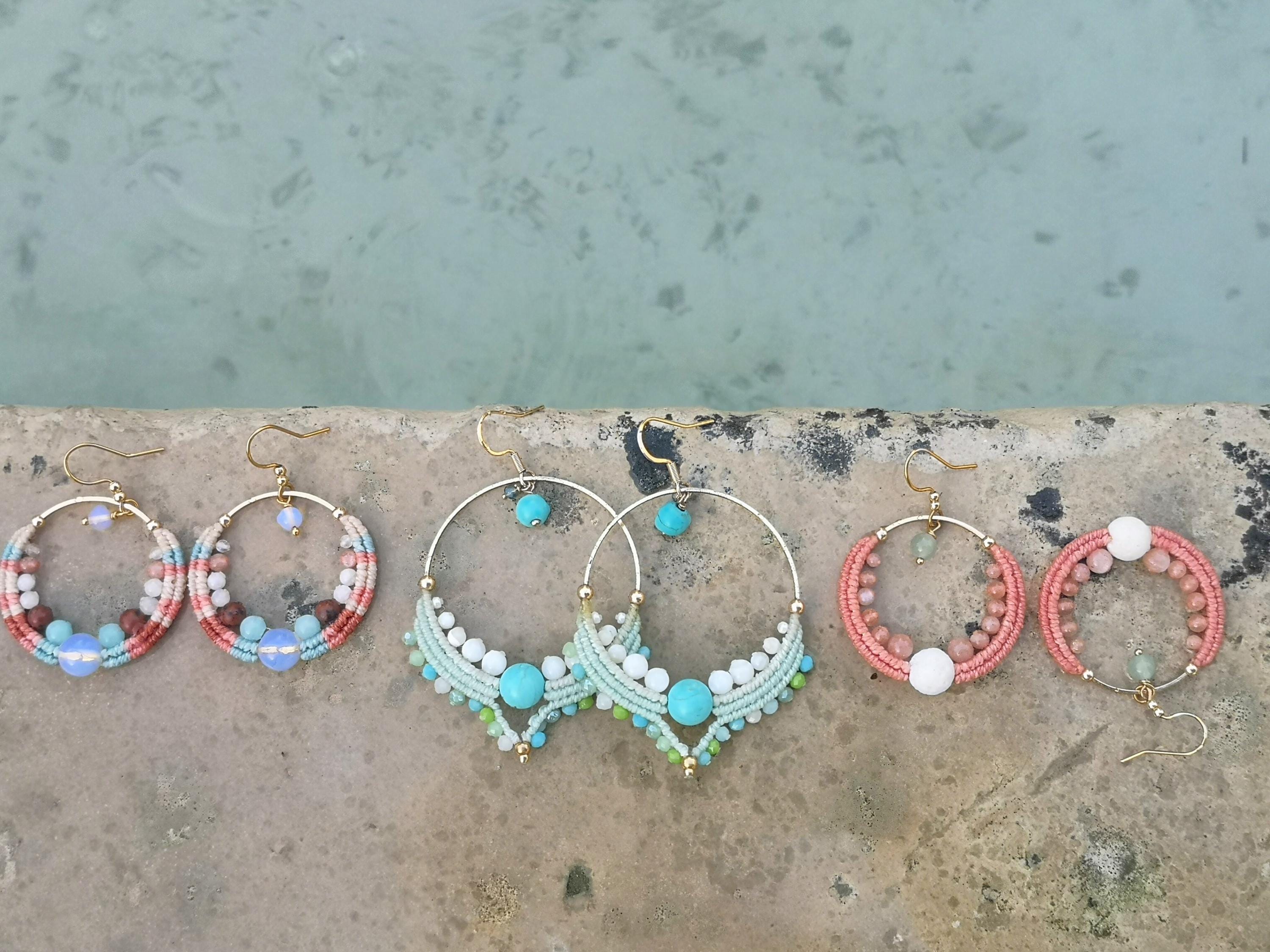 Peut inclure: Six paires de boucles d'oreilles créoles faites à la main avec des crochets dorés. Les boucles d'oreilles présentent divers motifs avec des perles colorées et des détails en macramé. Les couleurs incluent le corail, le turquoise, le blanc et le marron.