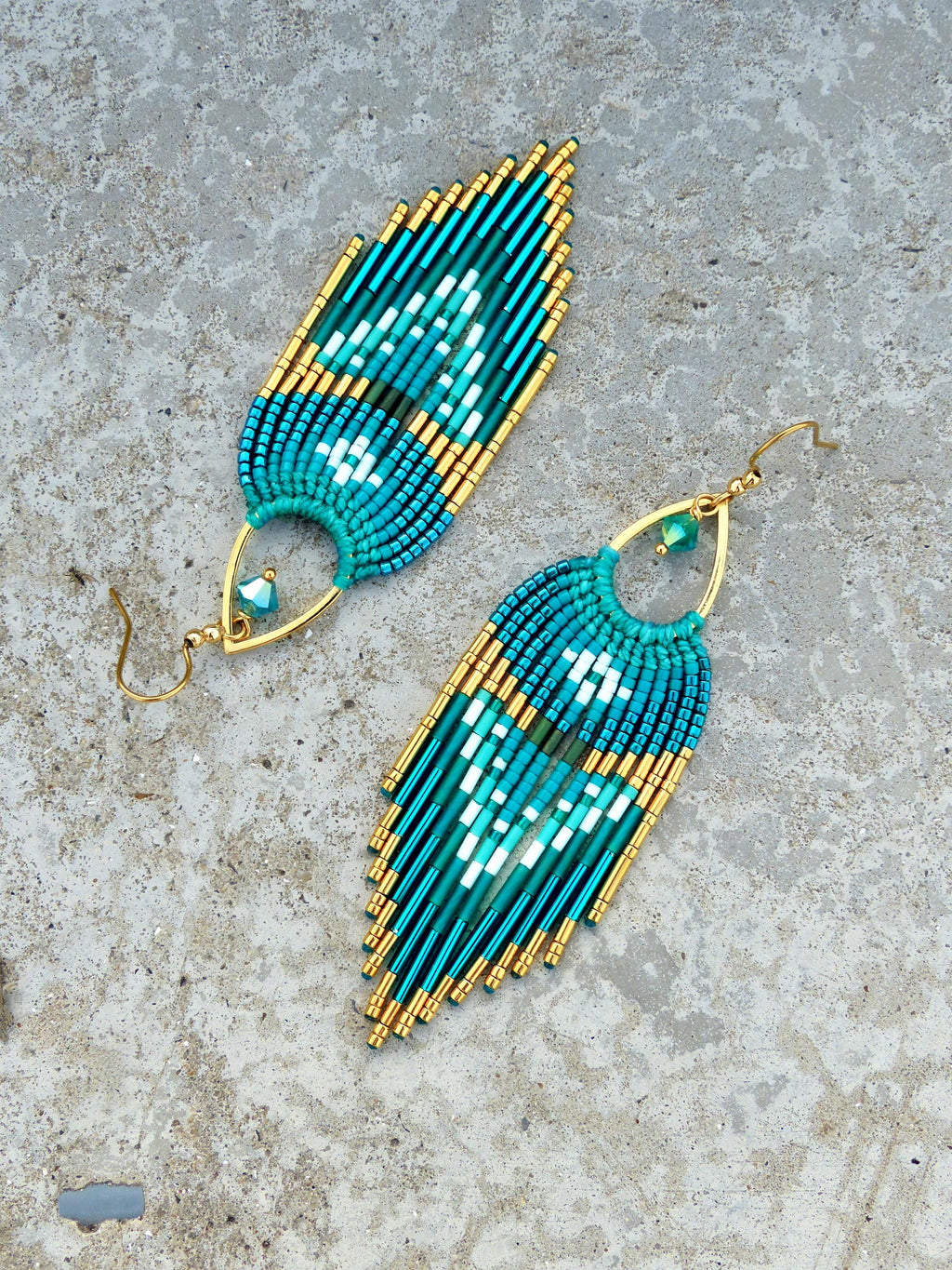 Peut inclure: Paire de boucles d'oreilles faites à la main en perles de couleur turquoise, bleu sarcelle et or. Les boucles d'oreilles présentent un motif en forme de plume avec un motif géométrique et sont suspendues à des crochets d'oreilles dorés.