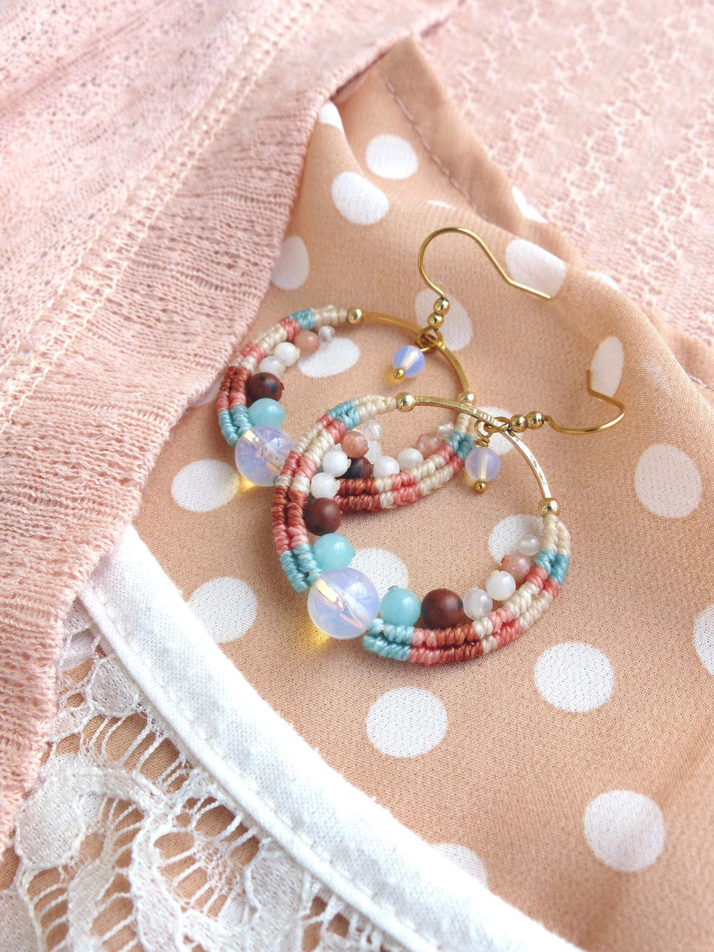 Peut inclure: Boucles d'oreilles créoles faites à la main avec un design macramé. Les boucles d'oreilles présentent une combinaison de couleurs, dont le rose, le bleu et le marron, et sont ornées de diverses perles. Les boucles d'oreilles ont des crochets dorés.