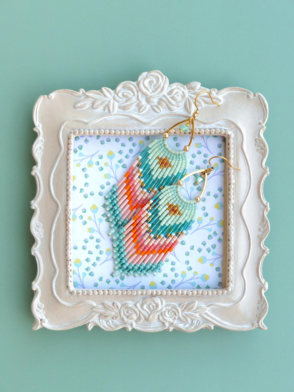 Peut inclure: Une paire de boucles d'oreilles en perles en forme de goutte d'eau avec un motif chevron dans des tons vert menthe, corail et orange. Les boucles sont composées de petites perles en verre et d'éléments en métal doré, incluant un crochet et un accent.
