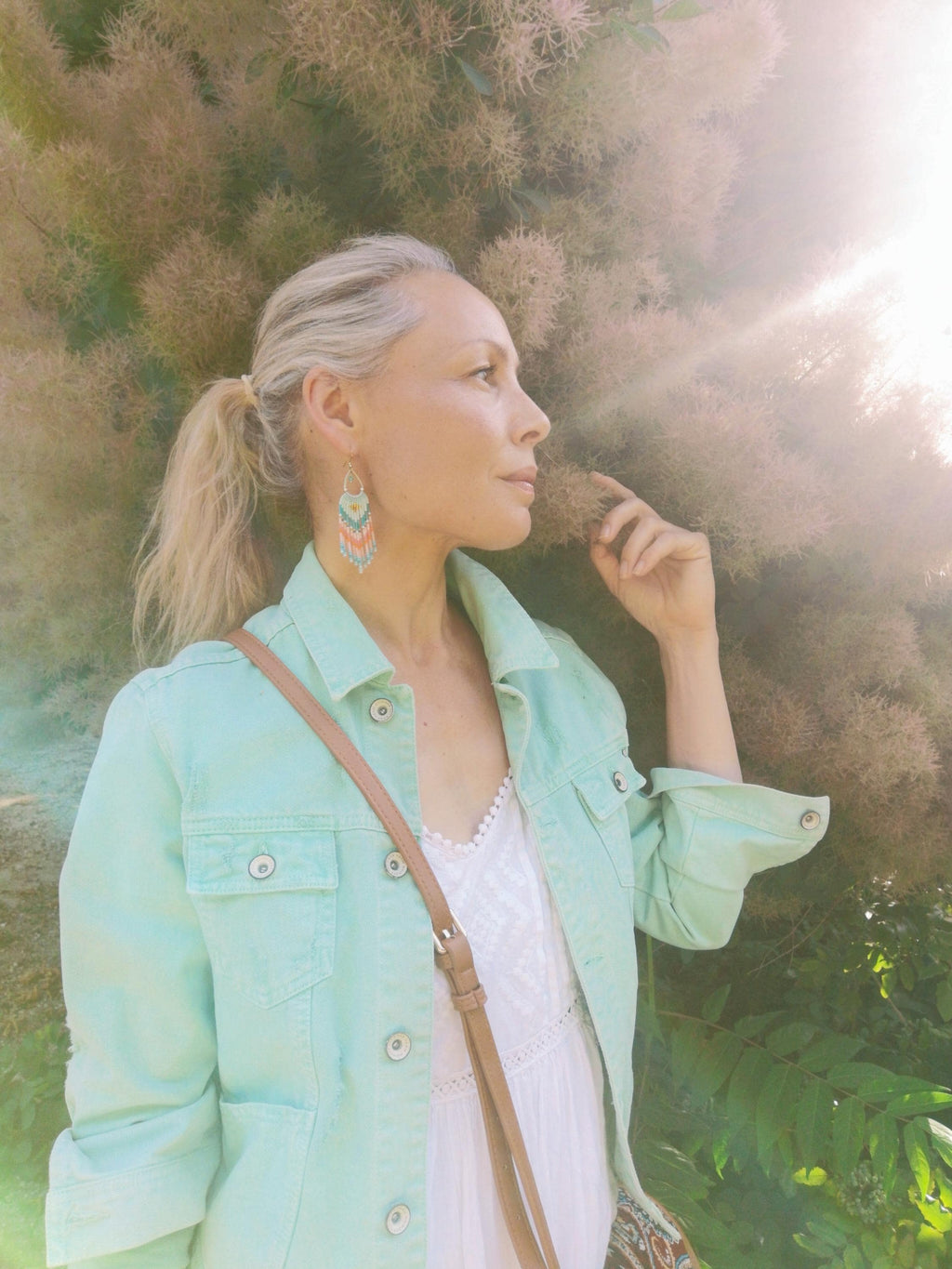 Peut inclure: Une paire de boucles d'oreilles à franges perlées en forme de goutte avec un motif géométrique dans des tons turquoise, blanc et corail, portées avec une veste en jean vert menthe clair sur un haut blanc et une bandoulière de sac beige.