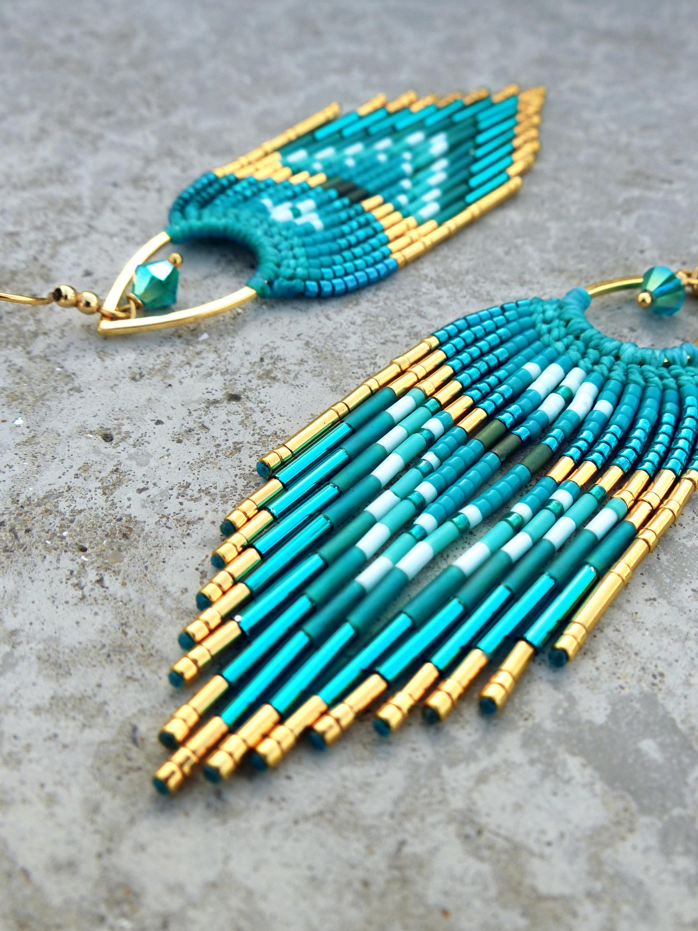 Peut inclure: Gros plan sur deux boucles d'oreilles faites à la main. Les boucles d'oreilles présentent un motif turquoise, sarcelle et or. Le design comprend une frange en forme d'éventail avec des accents dorés et un motif géométrique. Les boucles d'oreilles sont sur une surface grise.