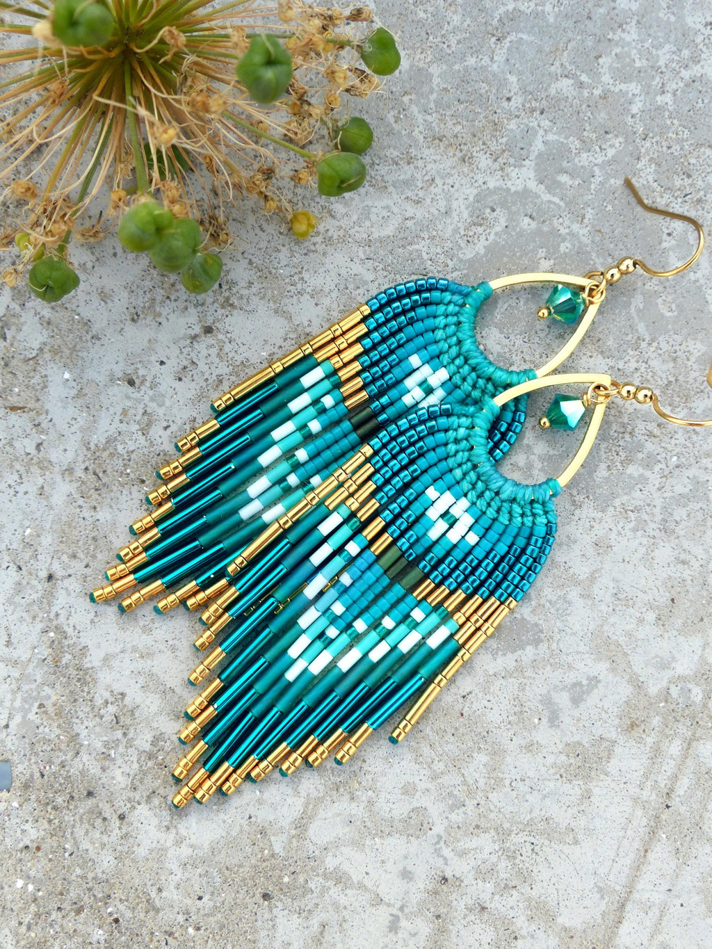 Peut inclure: Boucles d'oreilles en perles de couleur teal et or, avec un motif à franges. Les boucles d'oreilles présentent un motif géométrique blanc et teal, avec des accents dorés et des crochets d'oreilles. Mesurent environ 7.6 cm de long.