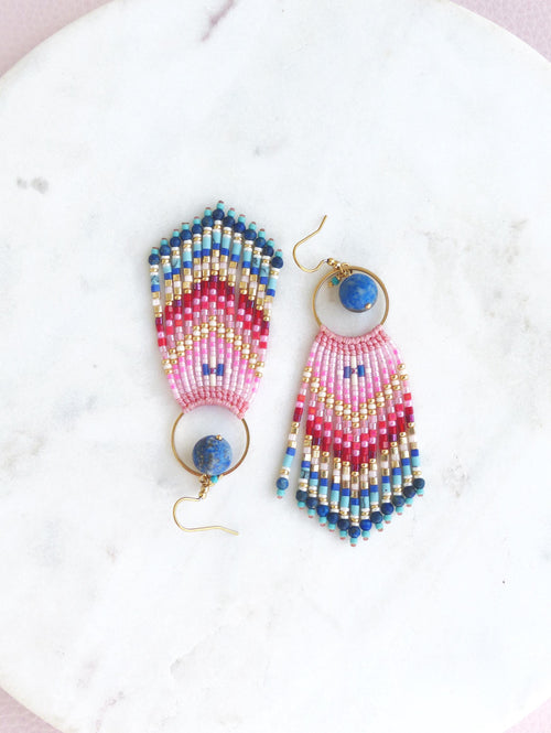 Peut inclure: Une paire de boucles d'oreilles pendantes composées d'un éventail de perles de rocaille multicolores dans des tons rose, rouge, bleu et doré. Chaque boucle comprend un anneau en métal doré avec une perle ronde en pierre bleue fixée.