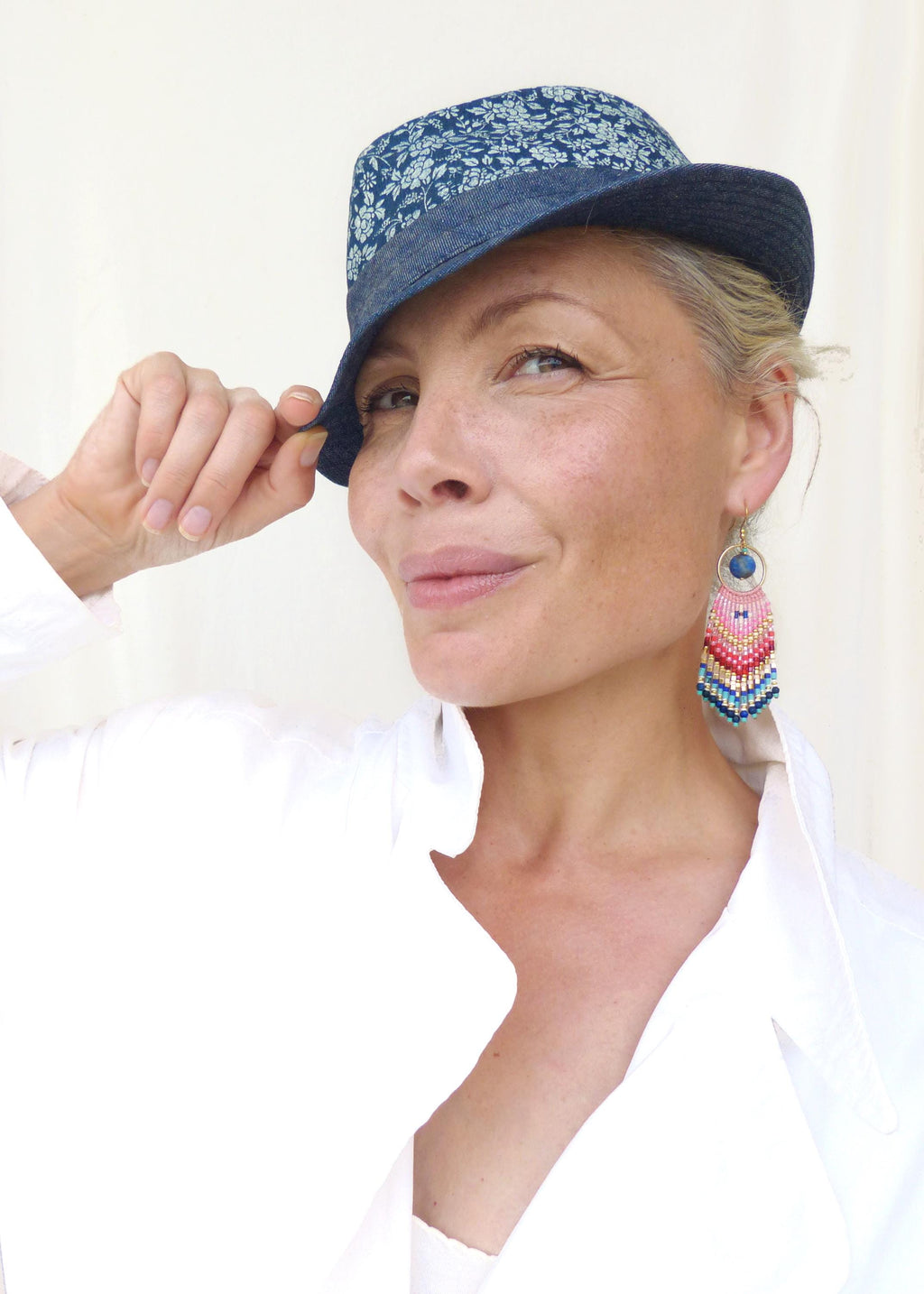 Peut inclure: Un chapeau fedora avec une calotte en tissu à motifs floraux bleus et blancs et un bord bleu uni. Une boucle d'oreille pendante composée d'un anneau doré, d'une perle bleu foncé et de franges perlées roses, rouges, blanches et bleues.