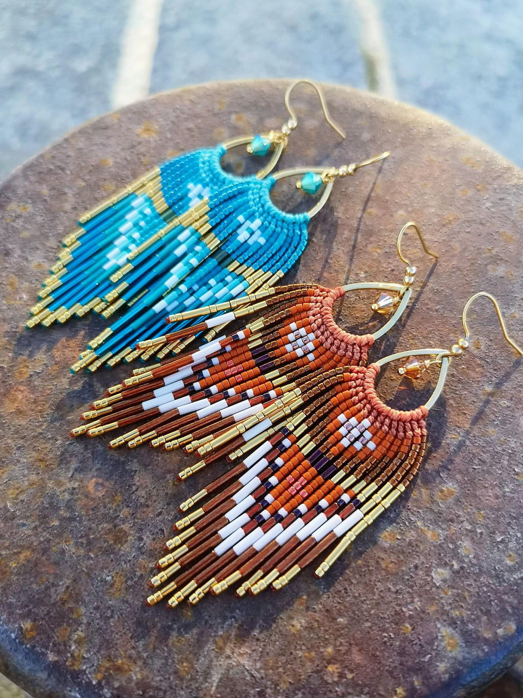 Peut inclure: Deux paires de boucles d'oreilles macramé faites à la main. Une paire est turquoise et dorée, l'autre est rouille, blanche et marron avec des accents dorés. Les boucles d'oreilles ont une forme de goutte d'eau avec des franges et des crochets dorés.
