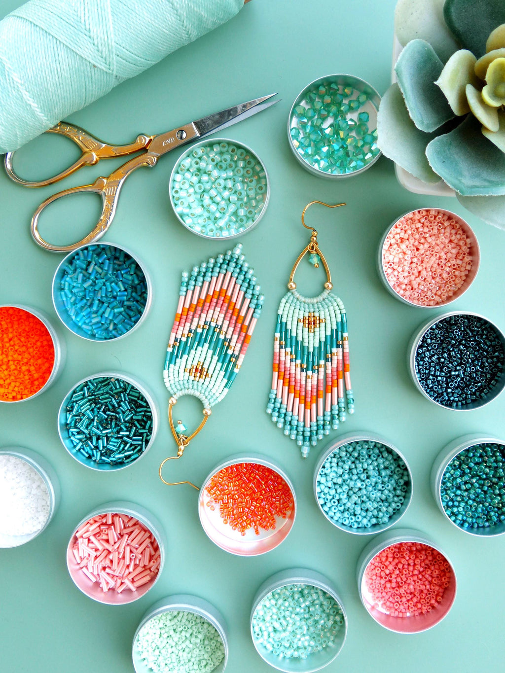 Peut inclure: Une paire de boucles d'oreilles à franges fabriquées à partir de petites perles en verre dans des tons vert menthe, corail et doré, avec une monture en métal doré en forme de goutte. Elles sont entourées de boîtes rondes remplies de perles.
