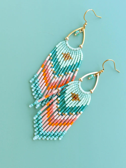 Peut inclure: Une paire de boucles d'oreilles pendantes avec des crochets dorés et des cadres en forme de goutte. Elles sont ornées de rangées de petites perles en verre dans des tons vert menthe, rose pâle et orange vif, formant un motif géométrique.