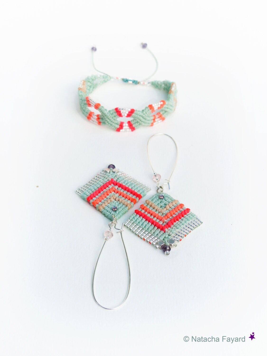 Peut inclure: Un ensemble de bijoux faits main comprenant un bracelet tissé vert, orange et blanc et une paire de boucles d'oreilles assorties. Les boucles d'oreilles sont de forme carrée et pendent de créoles argentées.