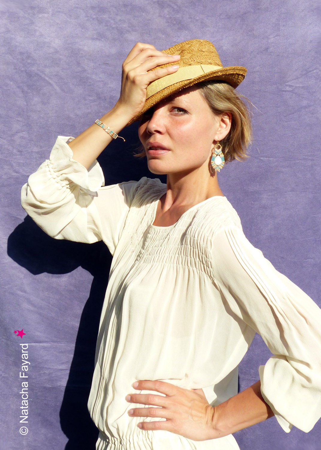 Peut inclure: Une femme portant une blouse blanche avec un col plissé et un chapeau de paille. Elle porte un bracelet et des boucles d'oreilles en perles turquoise et dorées.
