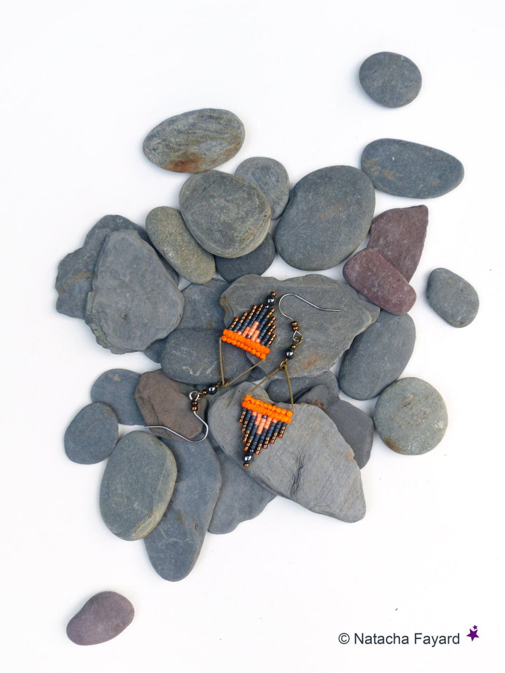 Peut inclure: Une paire de boucles d'oreilles en perles orange et noires avec un motif géométrique, disposées sur un lit de pierres grises.