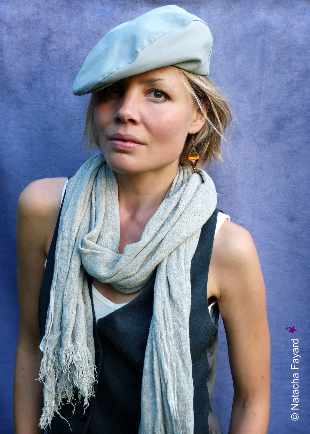 Peut inclure: Une femme portant une casquette plate grise, une écharpe gris clair et un haut noir sans manches. Elle porte des boucles d'oreilles orange et noires.