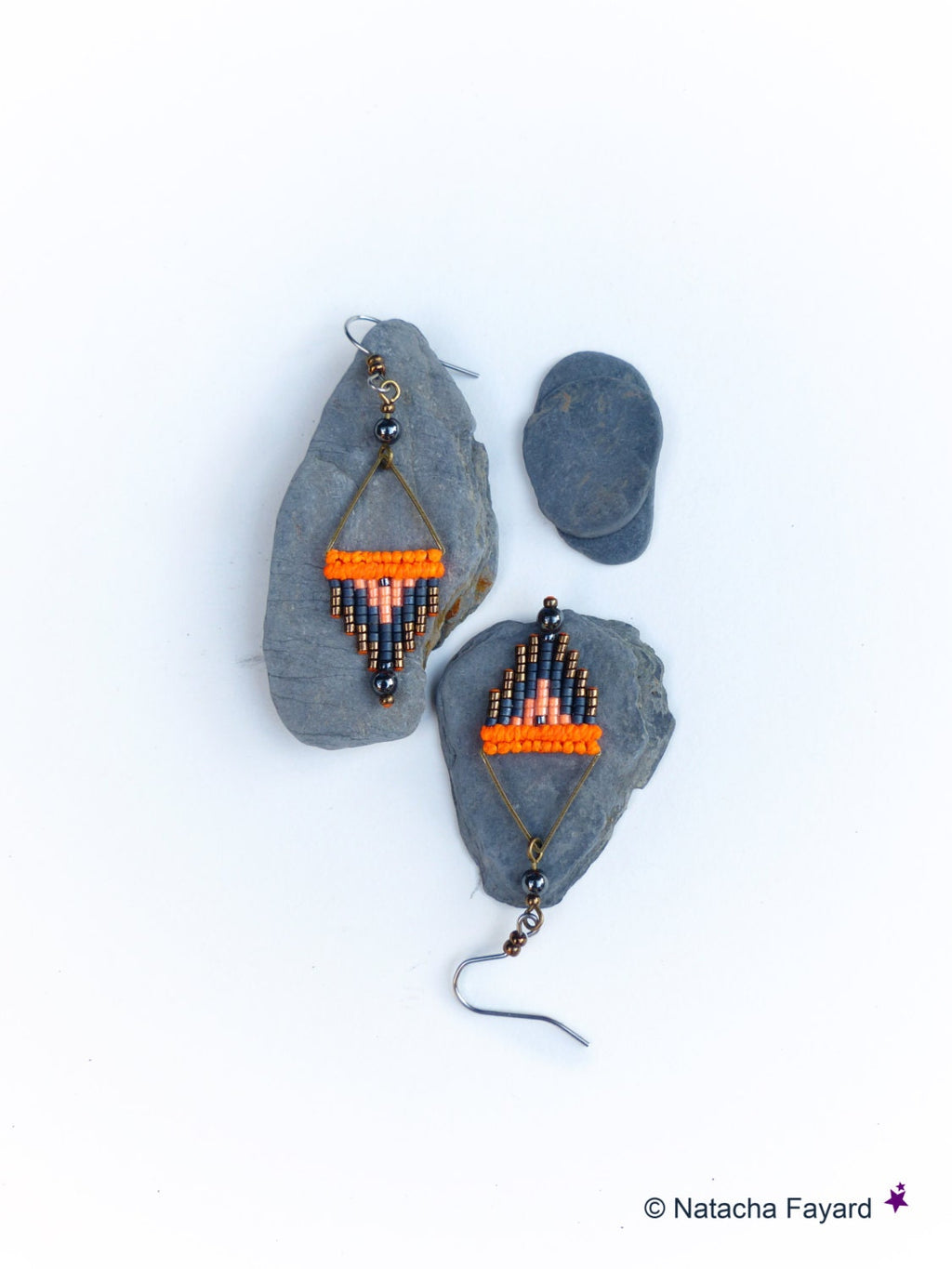 Peut inclure: Une paire de boucles d'oreilles en perles orange, noires et cuivre avec un motif géométrique. Les boucles d'oreilles sont suspendues à des pierres grises.