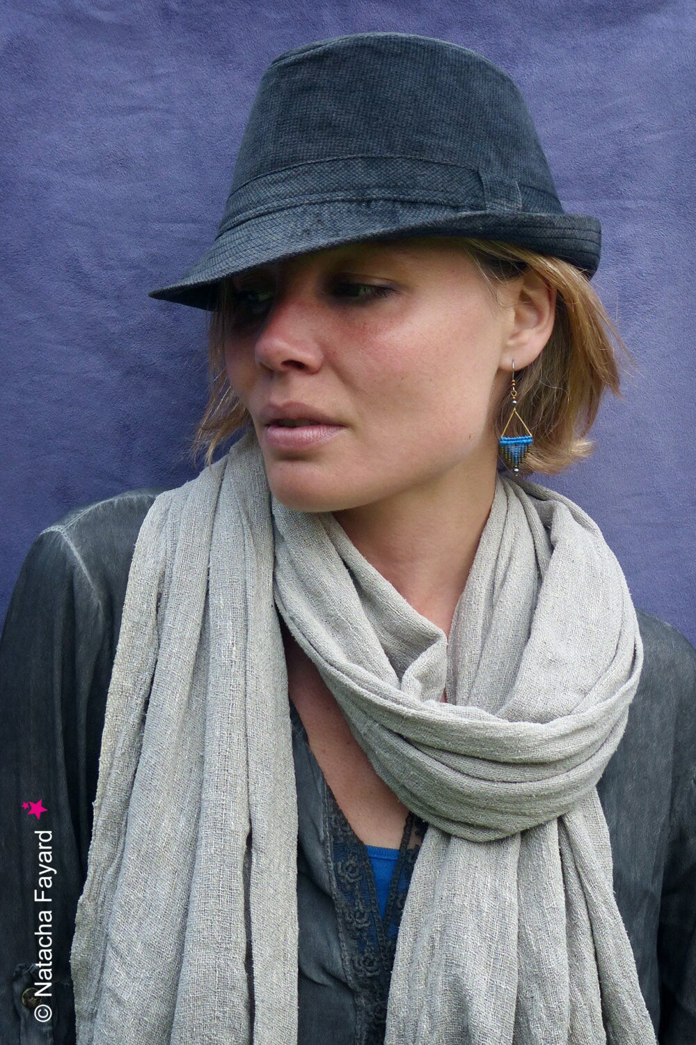 Peut inclure: Une femme portant une écharpe grise et un chapeau fedora noir avec une boucle d'oreille en perles bleues et dorées. 