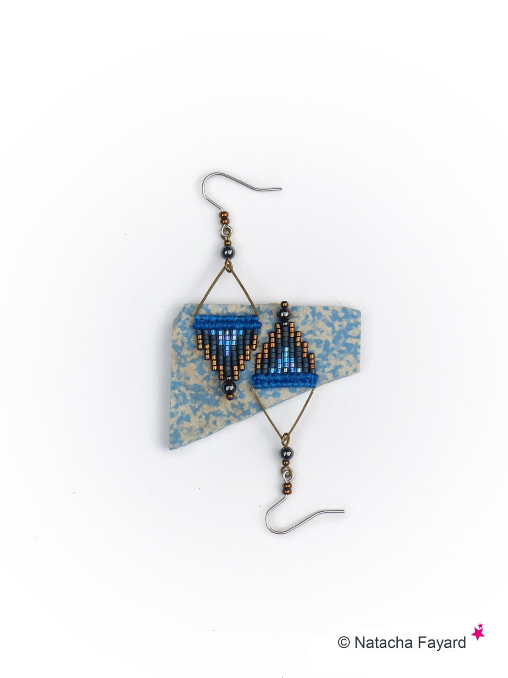 Peut inclure: Une paire de boucles d'oreilles en perles bleues et noires avec un motif géométrique. Les boucles d'oreilles sont suspendues à des crochets argentés.
