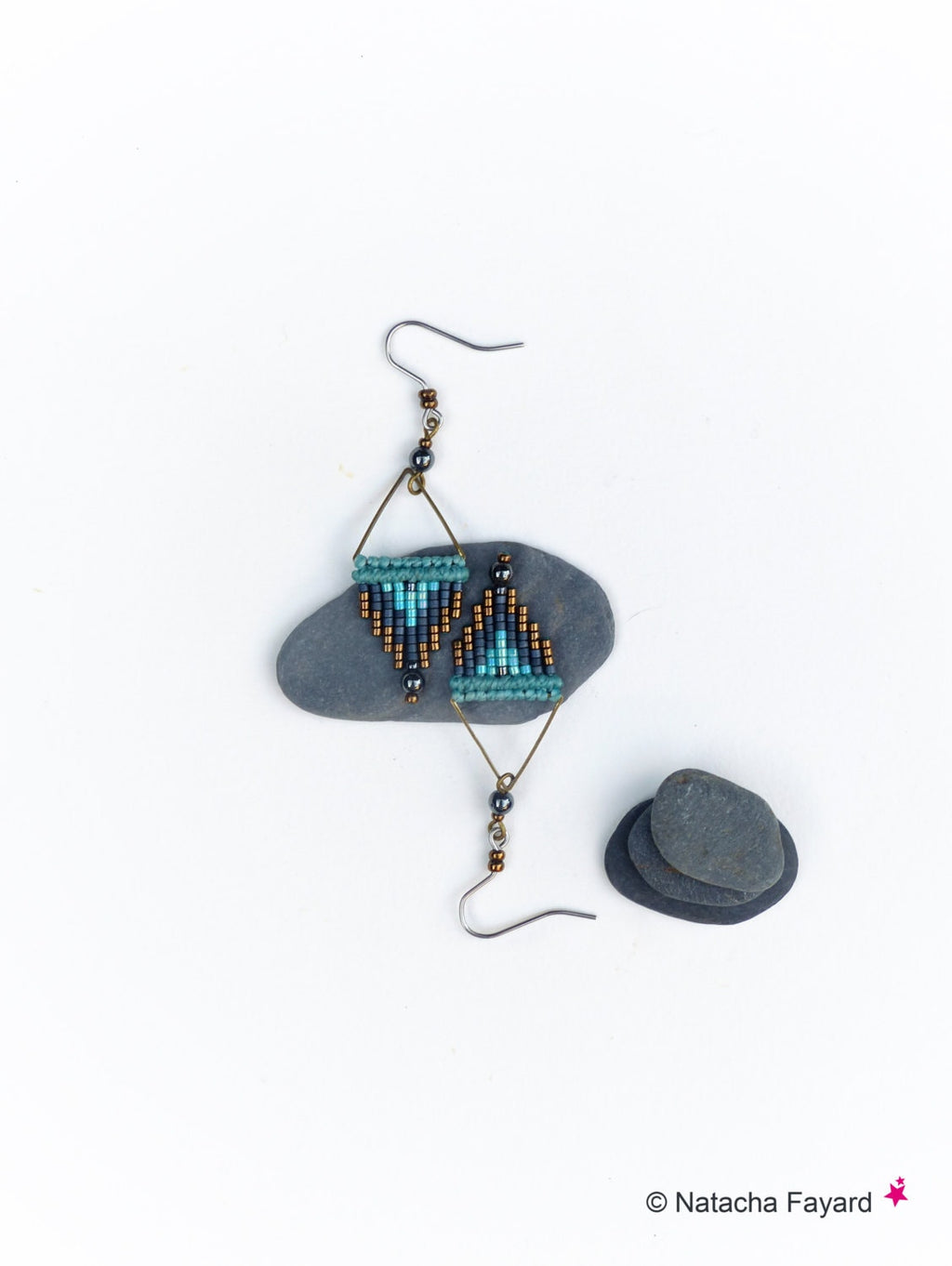 Peut inclure: Une paire de boucles d'oreilles en perles turquoise et argent avec un motif géométrique. Les boucles d'oreilles sont suspendues à un crochet argenté et sont présentées sur une pierre grise.