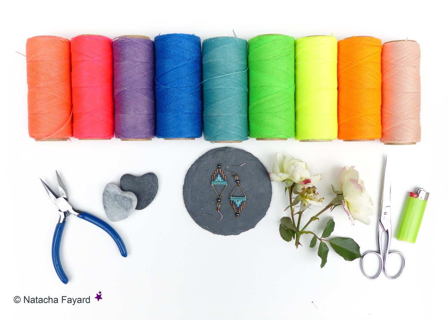 Peut inclure: Une vue de dessus de bobines de fil colorées, une paire de boucles d'oreilles en perles, un briquet, des ciseaux, des pinces et deux pierres en forme de cœur. 