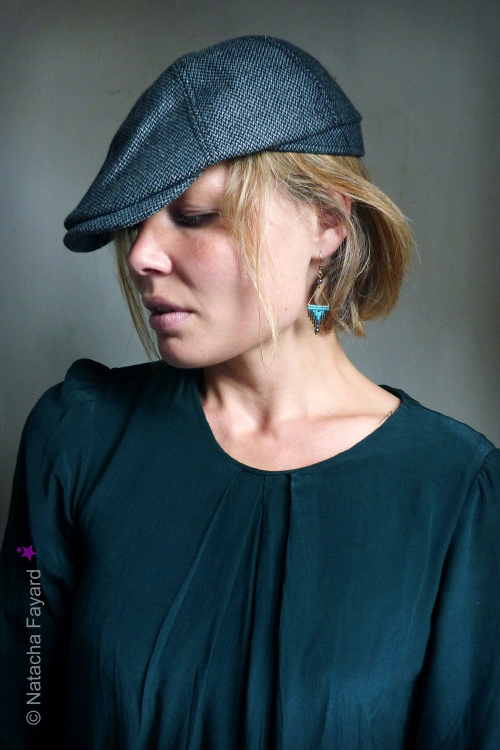 Peut inclure: Une femme portant une casquette de newsboy gris foncé et un chemisier vert foncé avec une boucle d'oreille turquoise triangulaire.